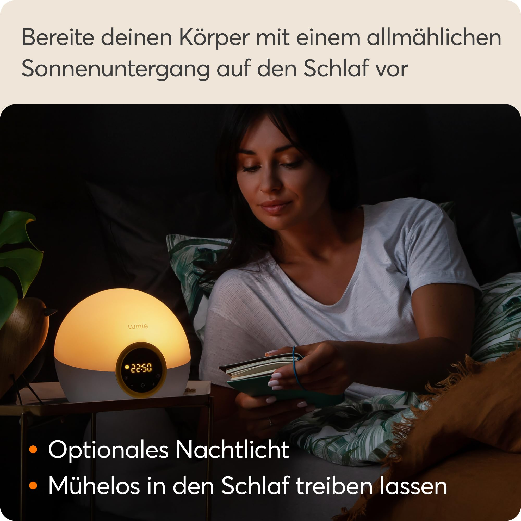 Eine Frau liest abends im Bett bei dem warmen Licht einer runden Lumie-Nachtlichtlampe.