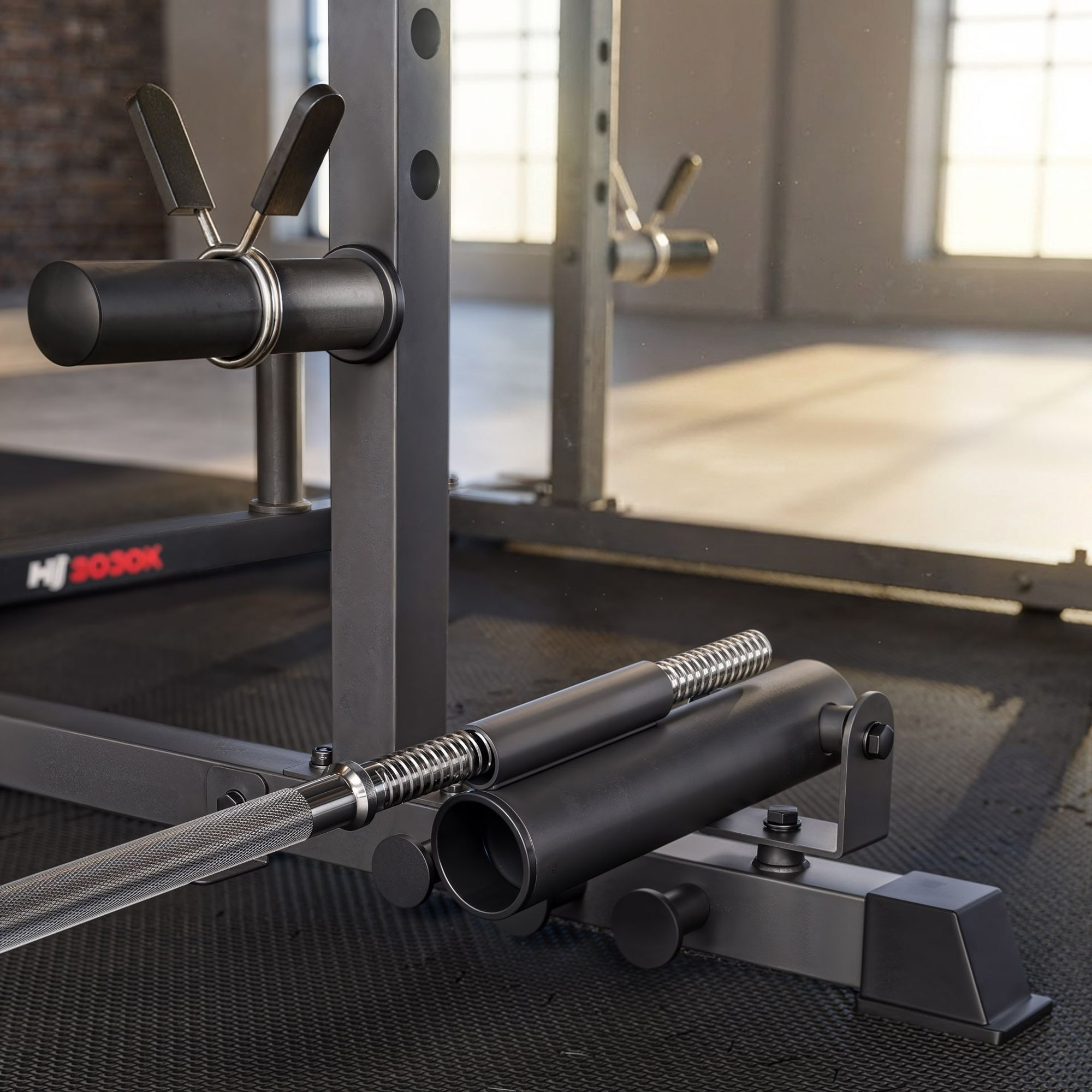 Nahaufnahme einer grauen Fitnessstation mit einer Langhantel am Boden in einem hellen, geräumigen Fitnessstudio.