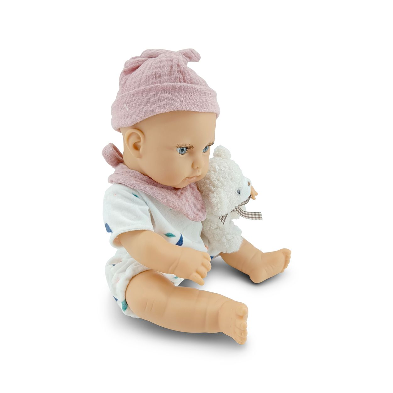 Eine Babypuppe mit rosa Mütze und Lätzchen sitzt und hält einen kleinen weißen Bären auf weißem Hintergrund.