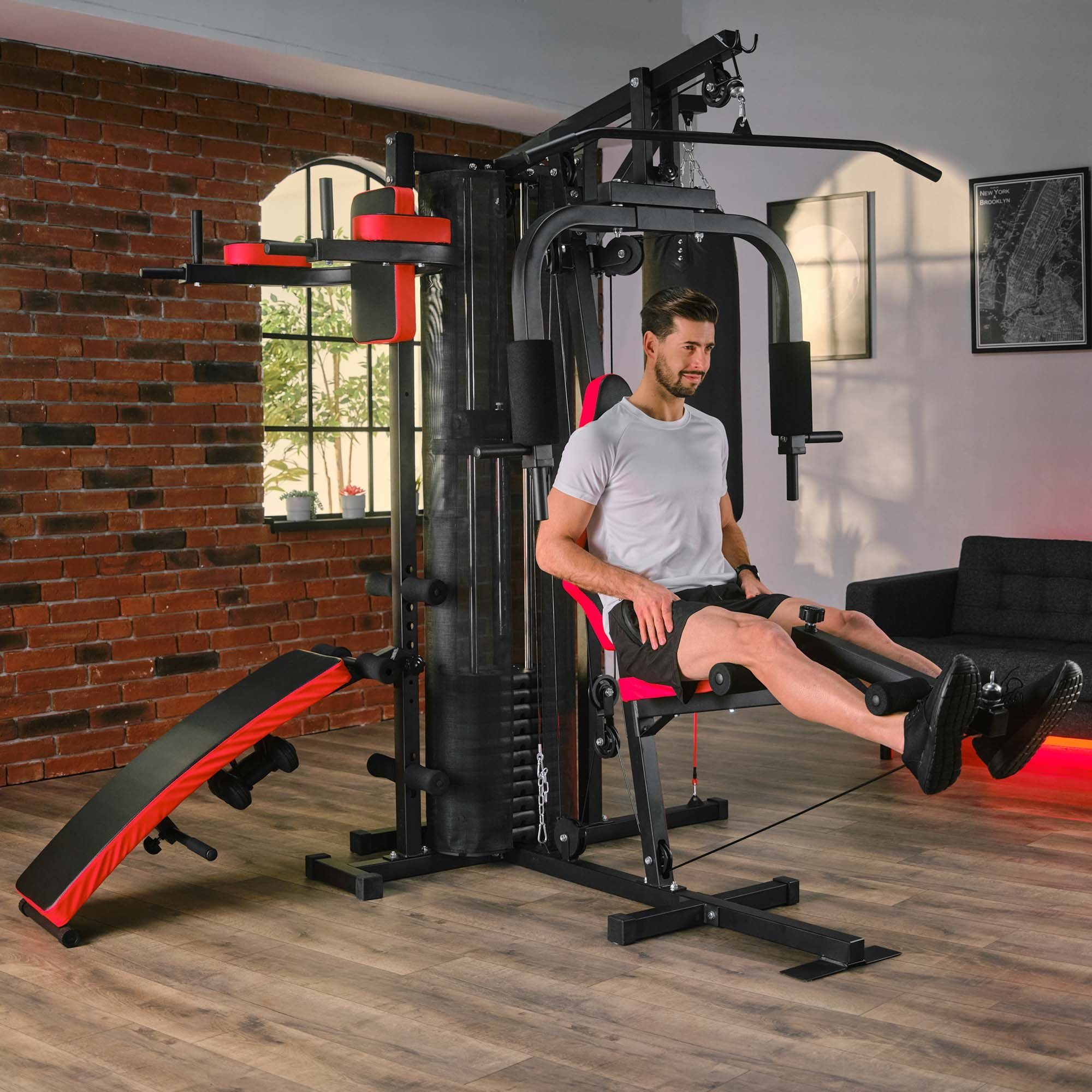 Ein Mann sitzt in einem modernen Fitnessstudio auf einer schwarzen und roten Multistation und trainiert.
