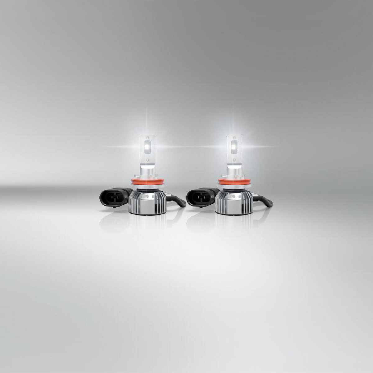Zwei beleuchtete LED-Scheinwerferlampen stehen auf einer glatten, grauen Oberfläche mit Reflektoren.