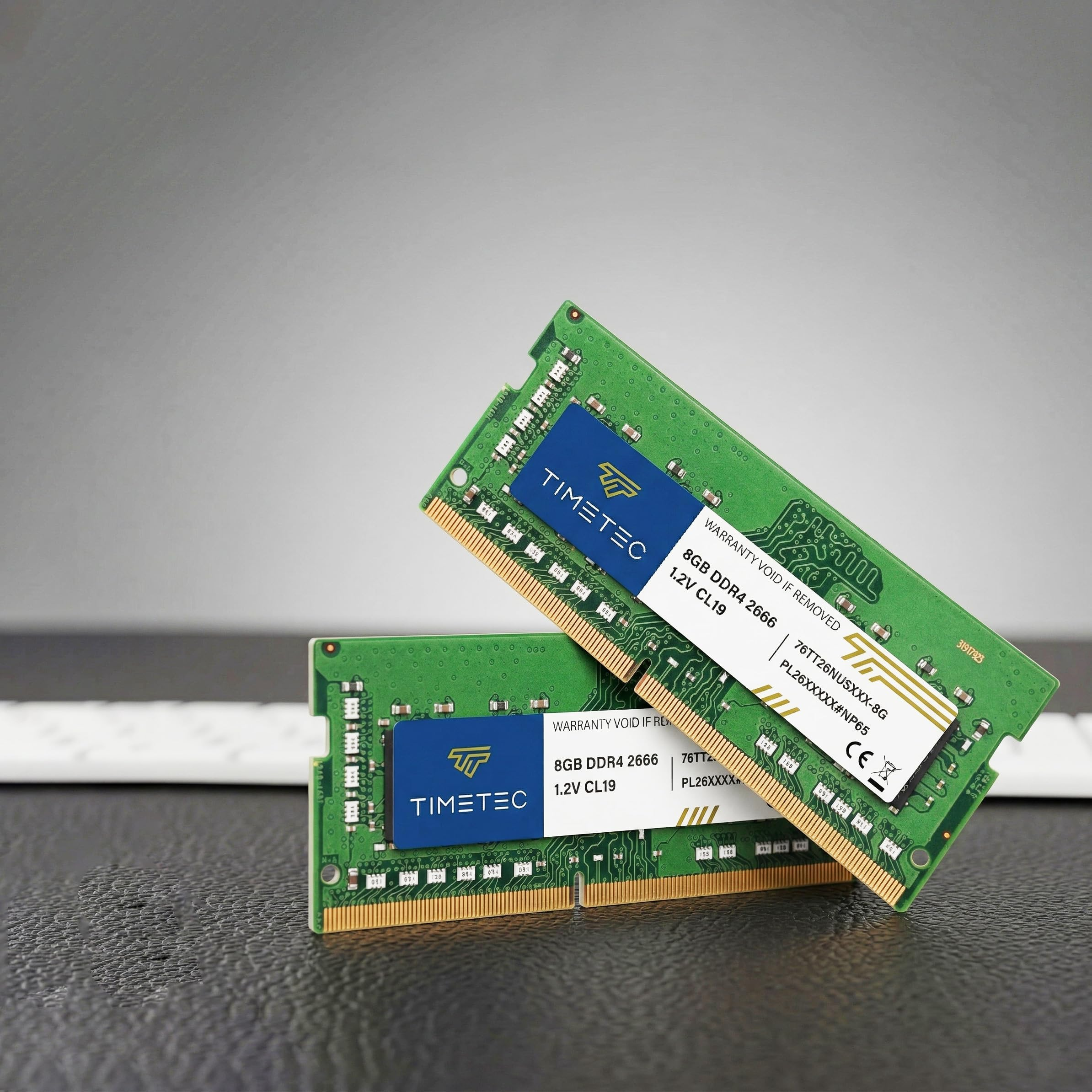 Zwei grüne Timetec 8GB DDR4 RAM-Stäbchen liegen auf einer dunklen Oberfläche vor grauem Hintergrund.