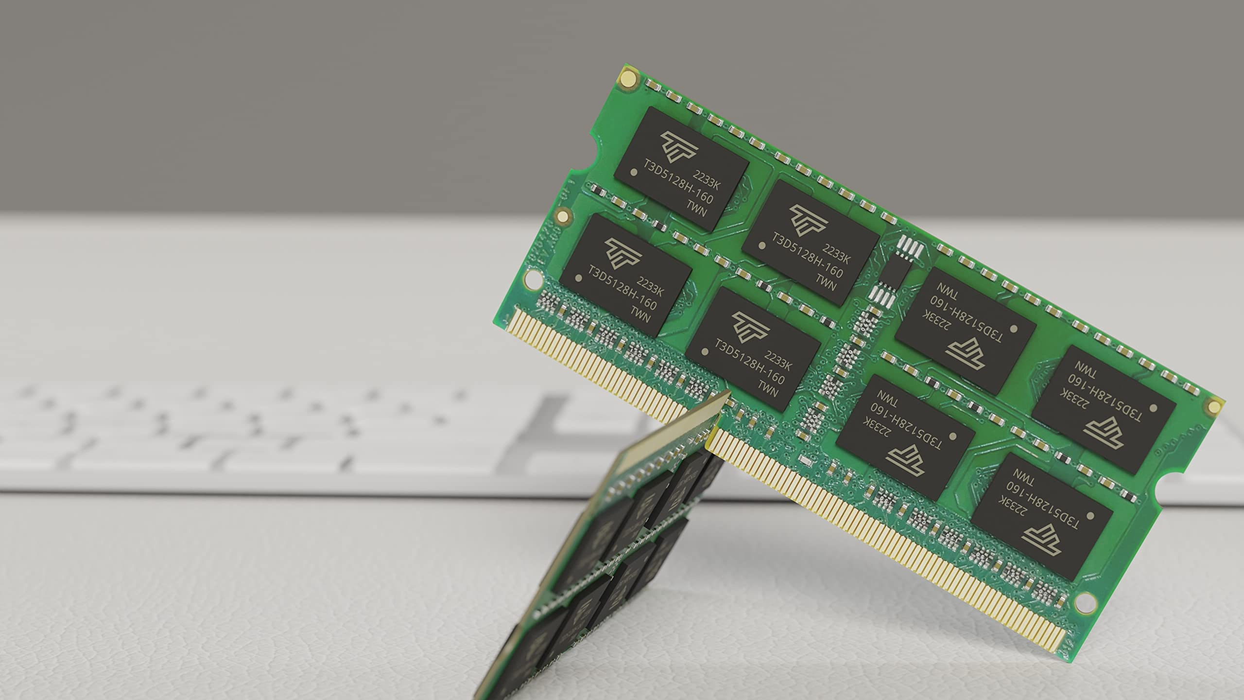 Deux modules RAM verts posés sur une surface blanche, avec un clavier flou en arrière-plan.