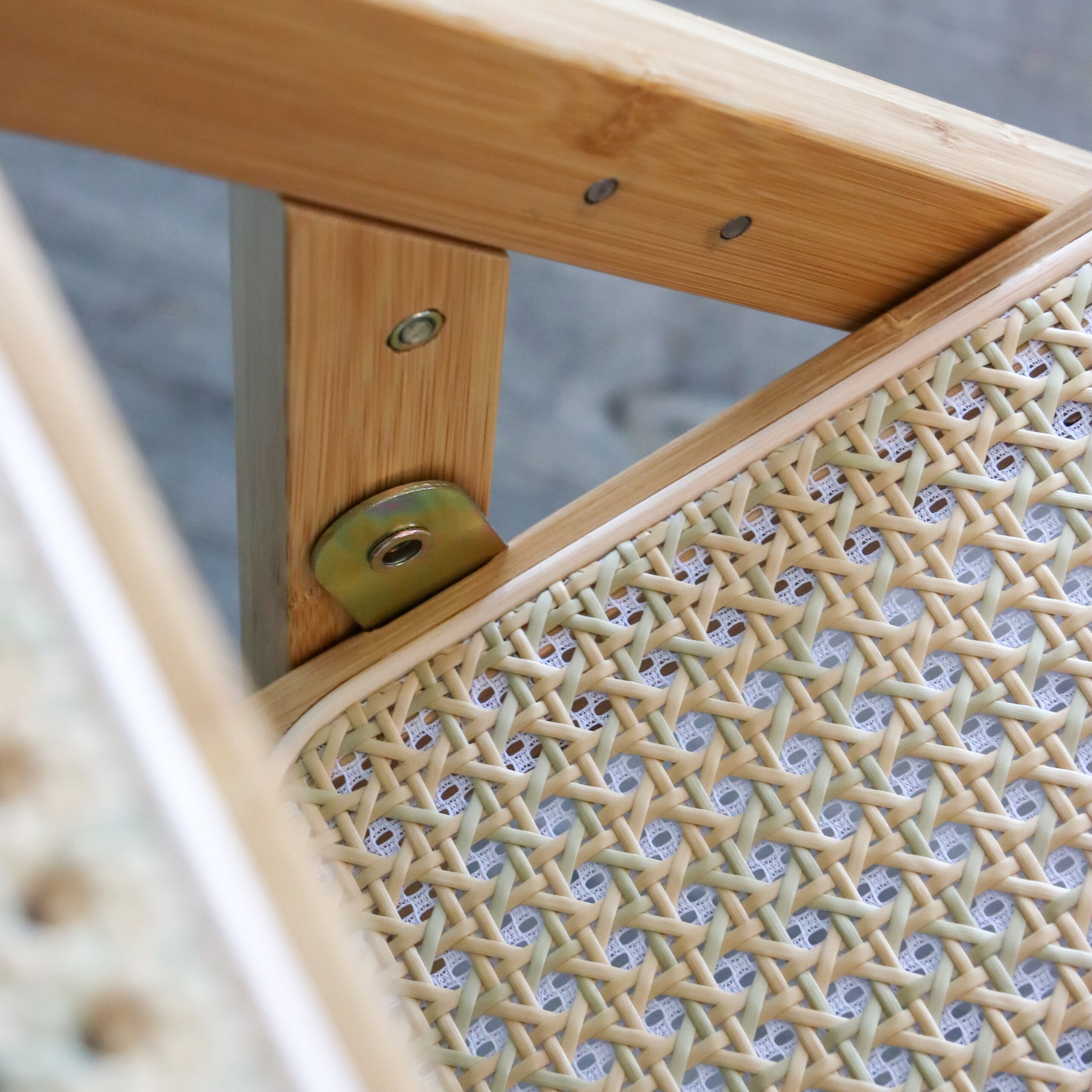 Nahaufnahme einer Holzstuhlverbindung mit Metallwinkel und Rattansitz.