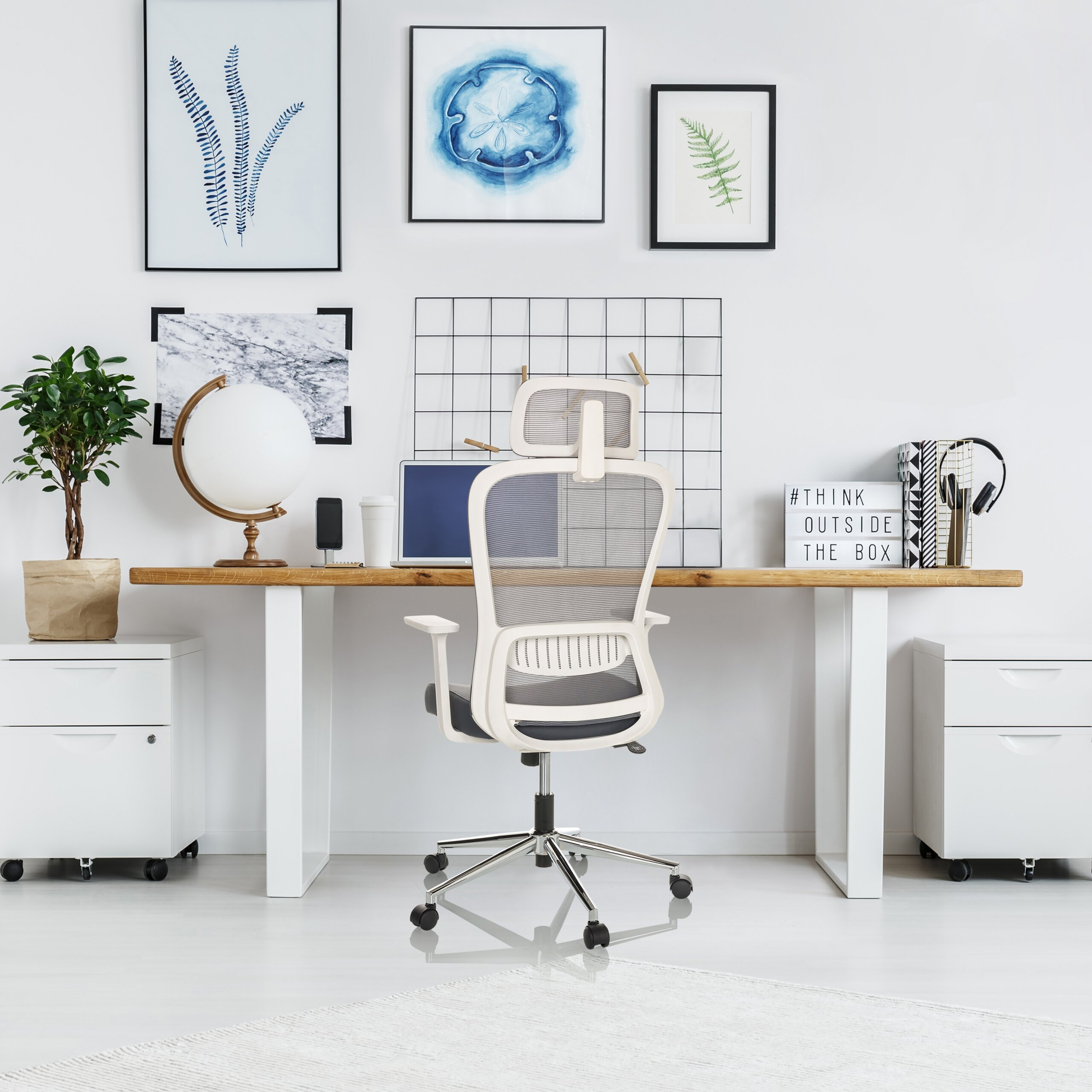 Moderne Büroinstallation mit hellem Holztisch, weißem Stuhl, Pflanzen, Globus und gerahmten Kunstdrucken.