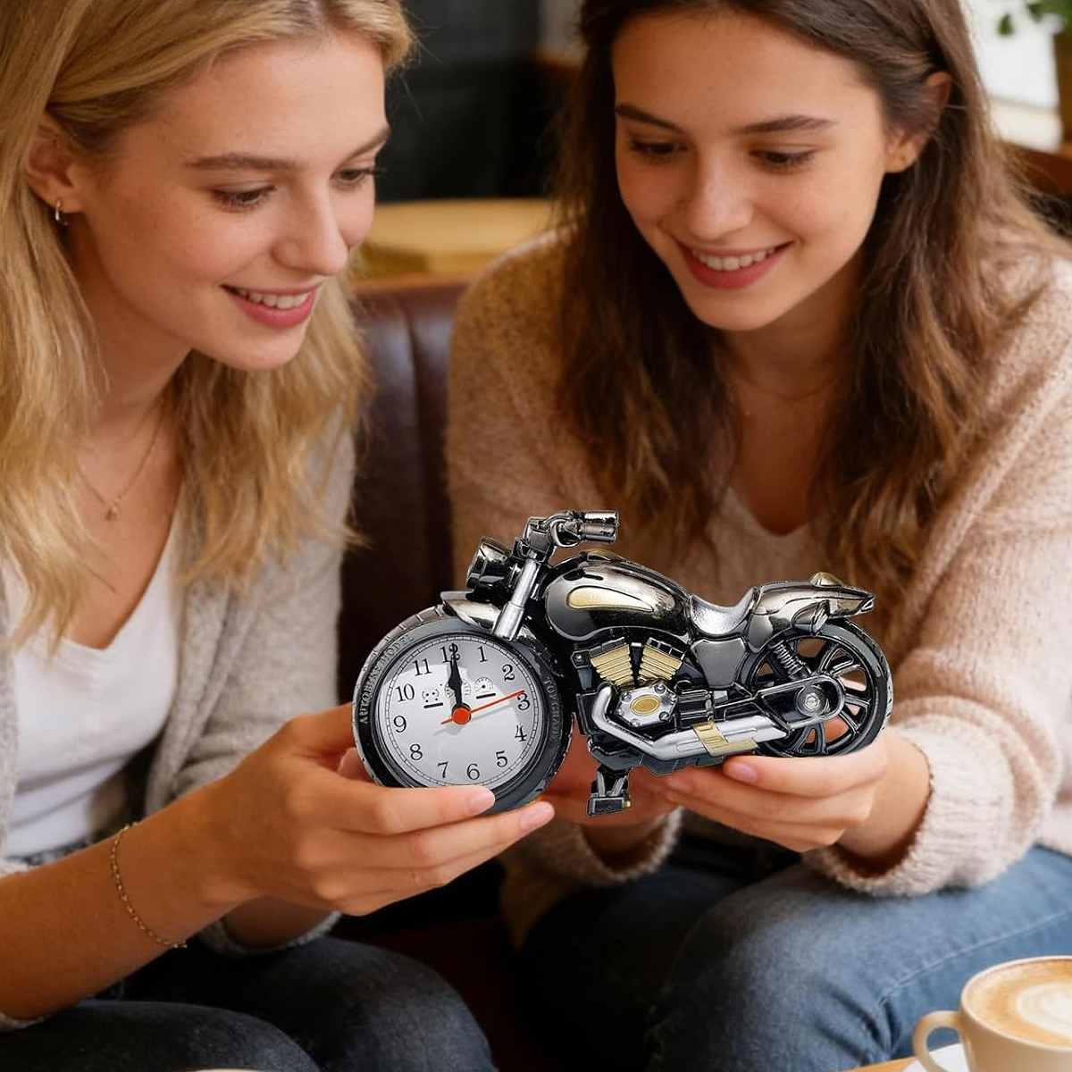 Zwei junge Frauen betrachten lächelnd einen kleinen Motorrad-Wecker.