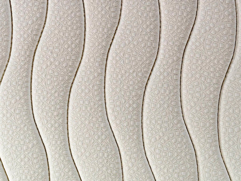 Primer plano de un colchón de color crema con patrones de ondas verticales y acolchado geométrico.