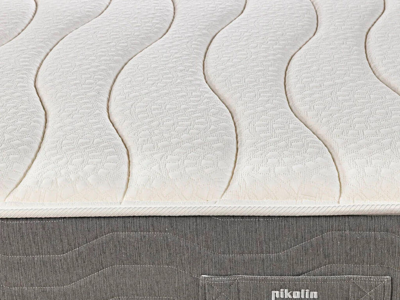 Primer plano de un colchón blanco con patrón de ondas y borde de tela gris.