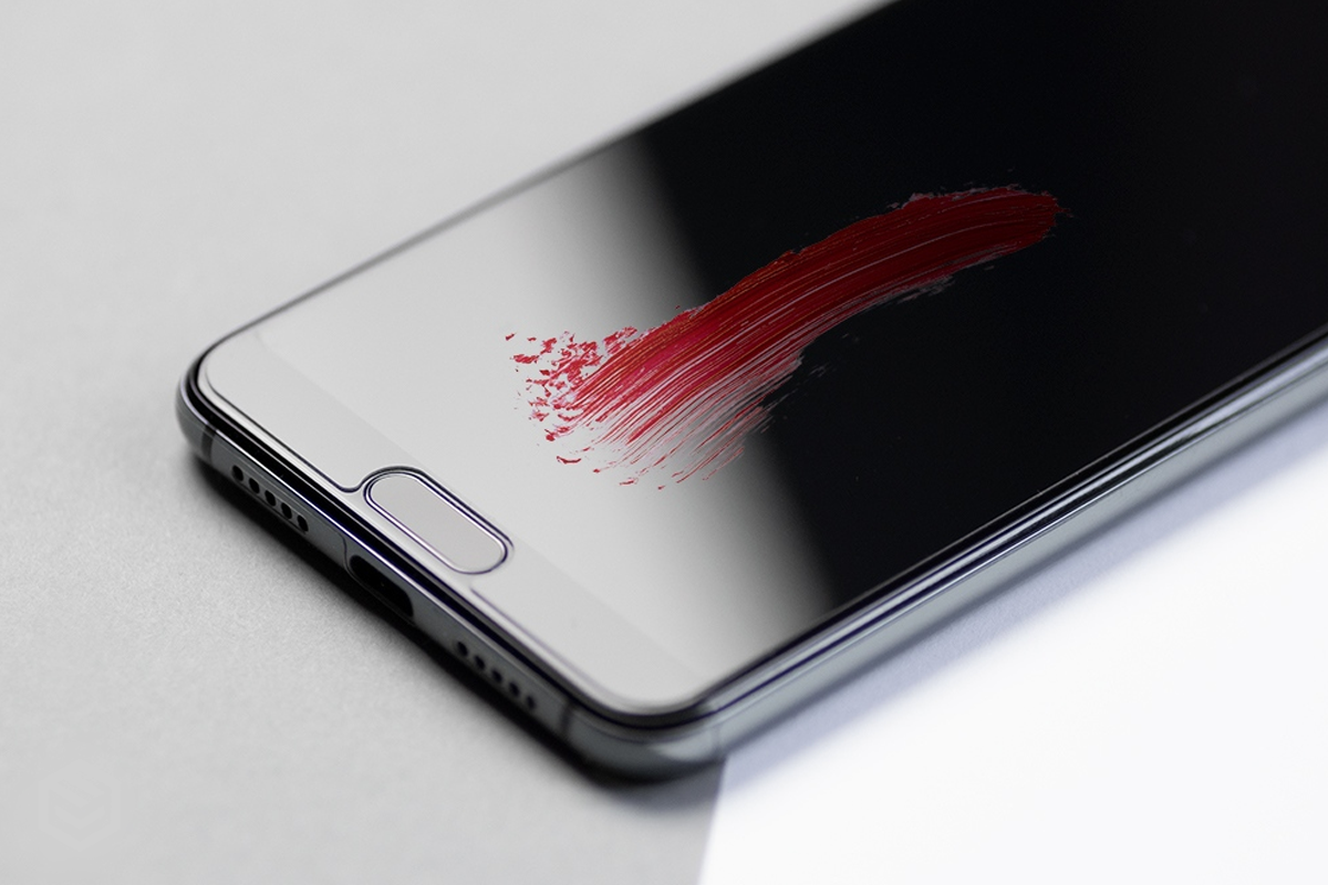 Ciemny smartfon na szarym tle z czerwonym śladem szminki na ekranie.