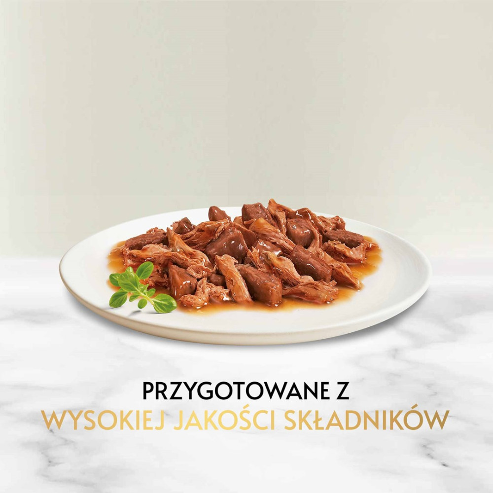 Biały talerz z gotowanym, szarpanym mięsem w sosie i zielonymi ziołami na jasnym tle.