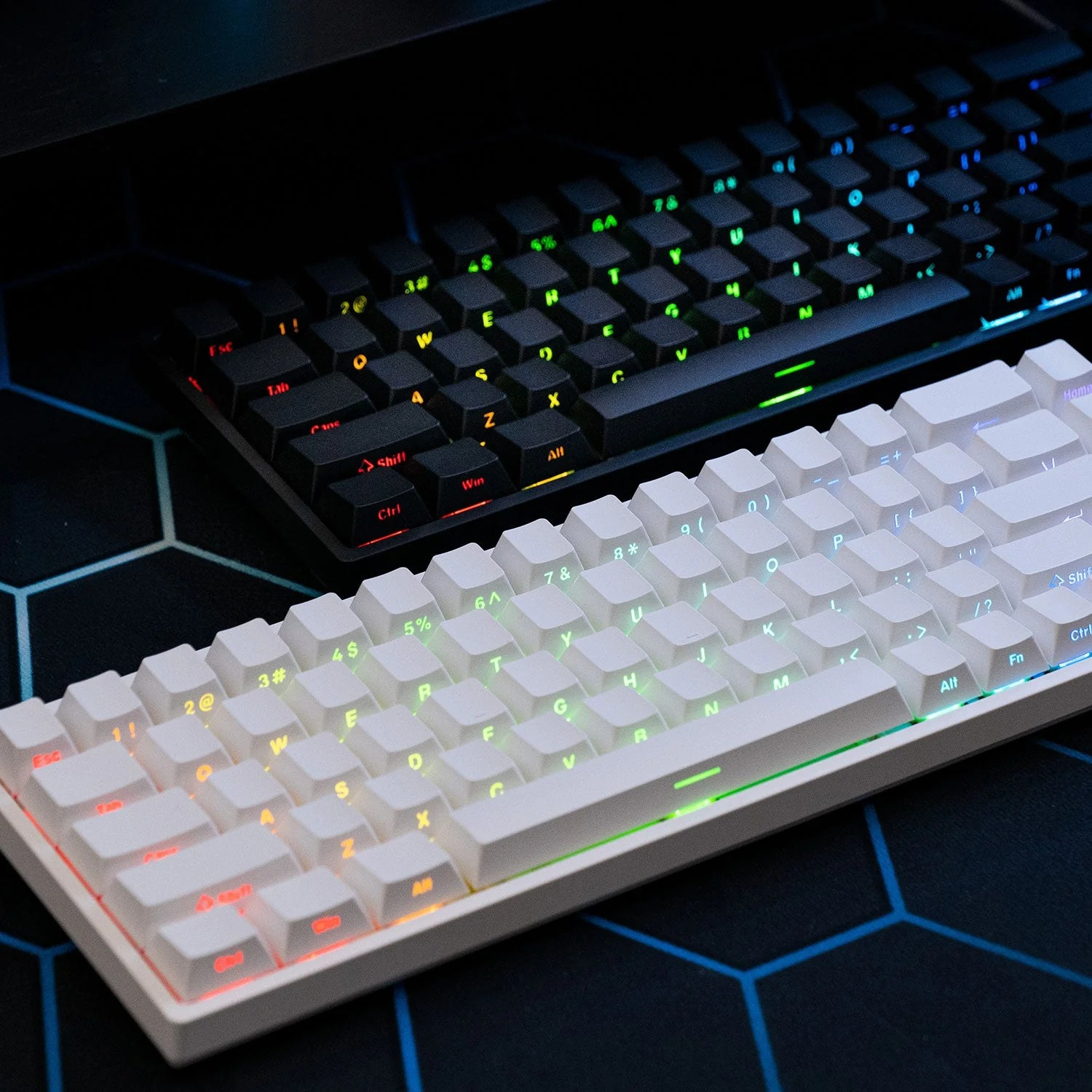 Dwie mechaniczne klawiatury RGB, biała i czarna, leżą na niebieskiej podkładce w motyw plastra miodu.
