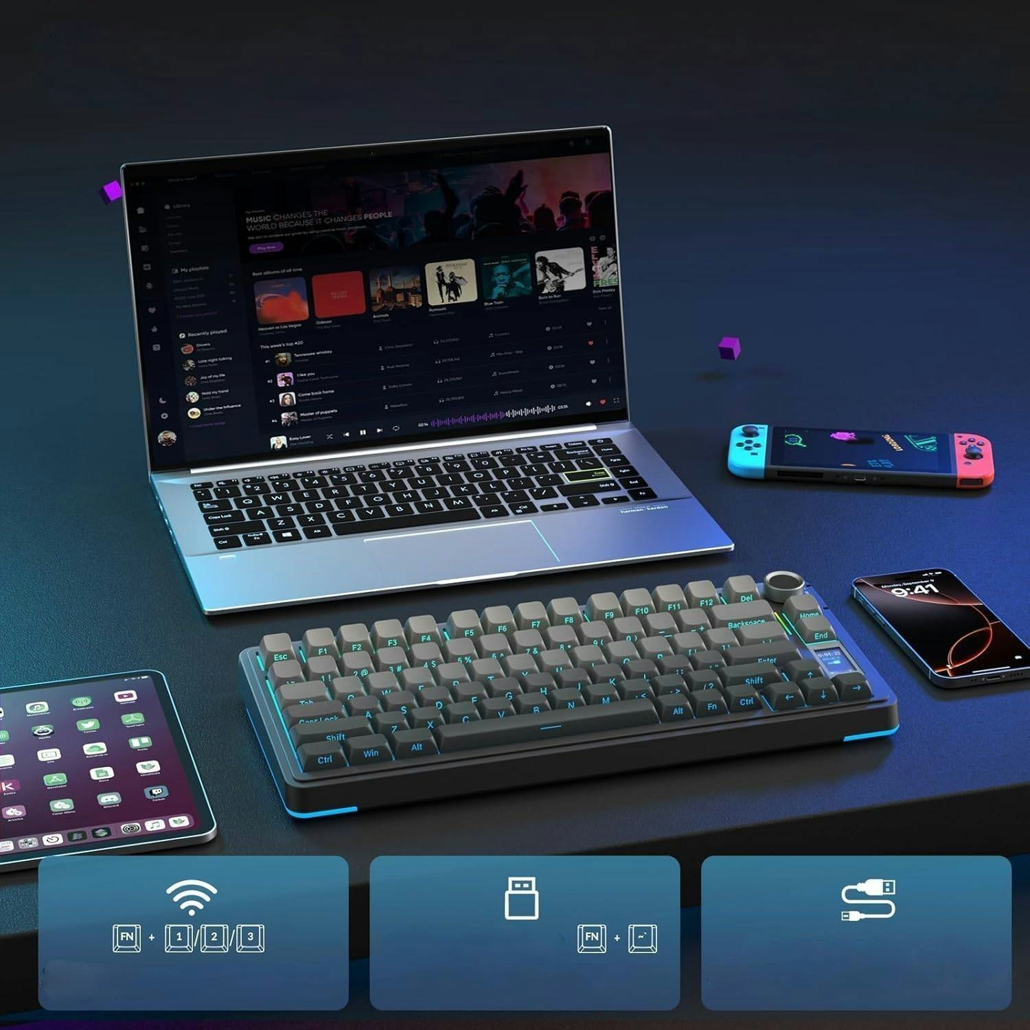 Podswietlony laptop, osobna klawiatura, tablet, smartfon i konsola przenosna na ciemnym biurku.