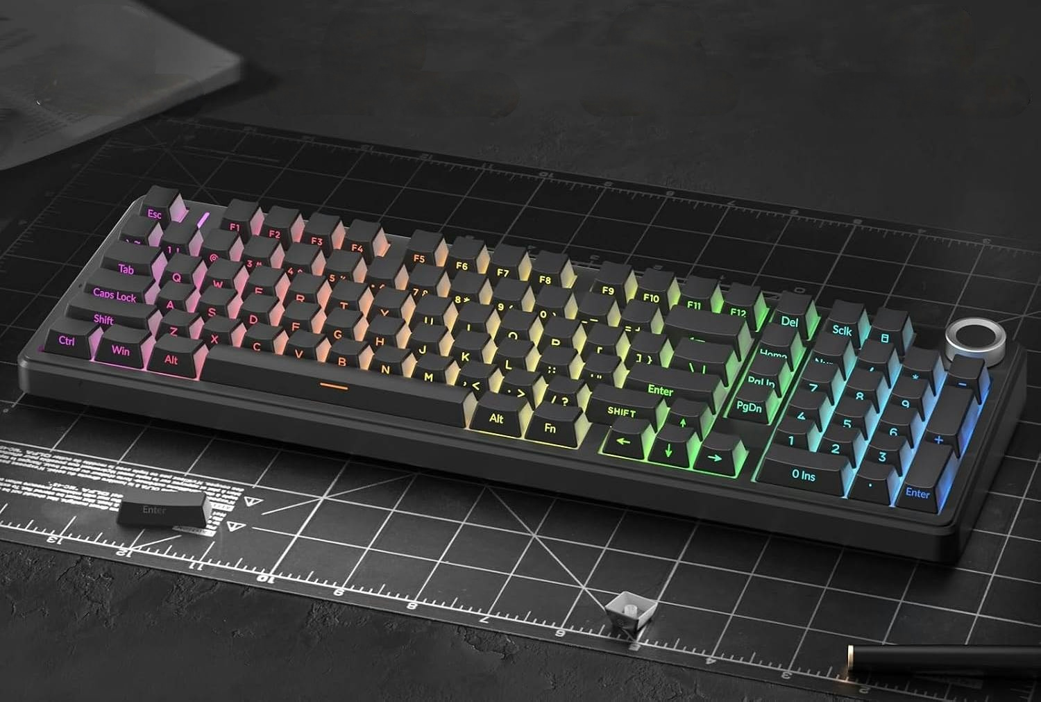 Czarna klawiatura mechaniczna z wielokolorowym podświetleniem RGB leży na czarnej macie do cięcia.