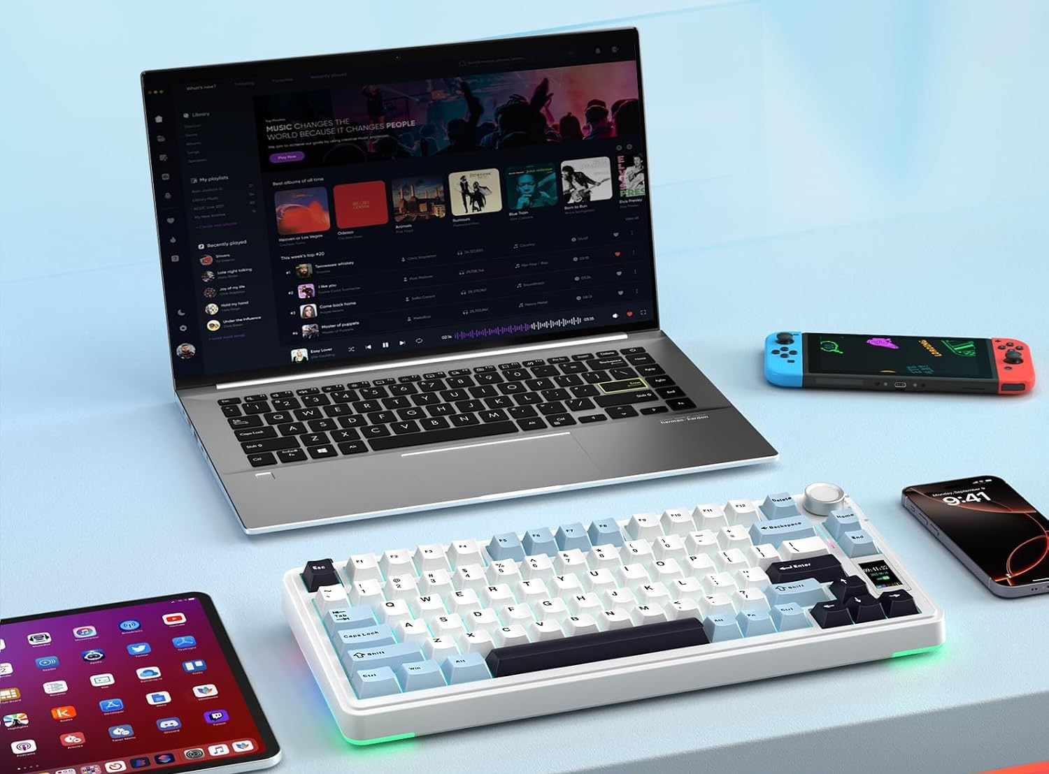 Laptop, klawiatura bezprzewodowa, tablet, smartfon i konsola przenośna na niebieskim tle.