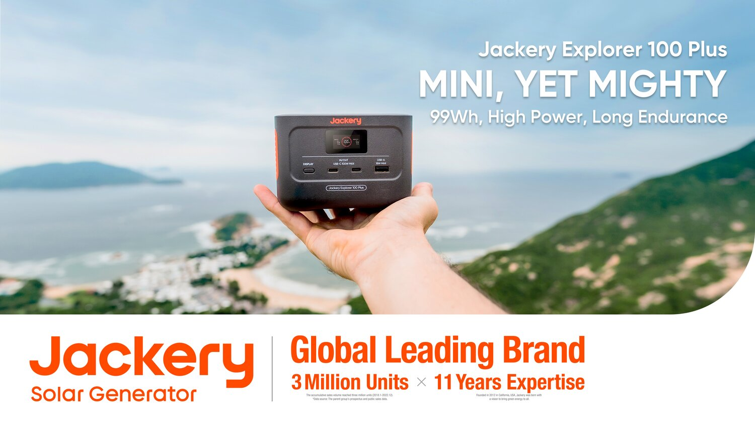 Una mano regge una piccola centrale elettrica Jackery Explorer 100 Plus su uno sfondo di montagna e costa.