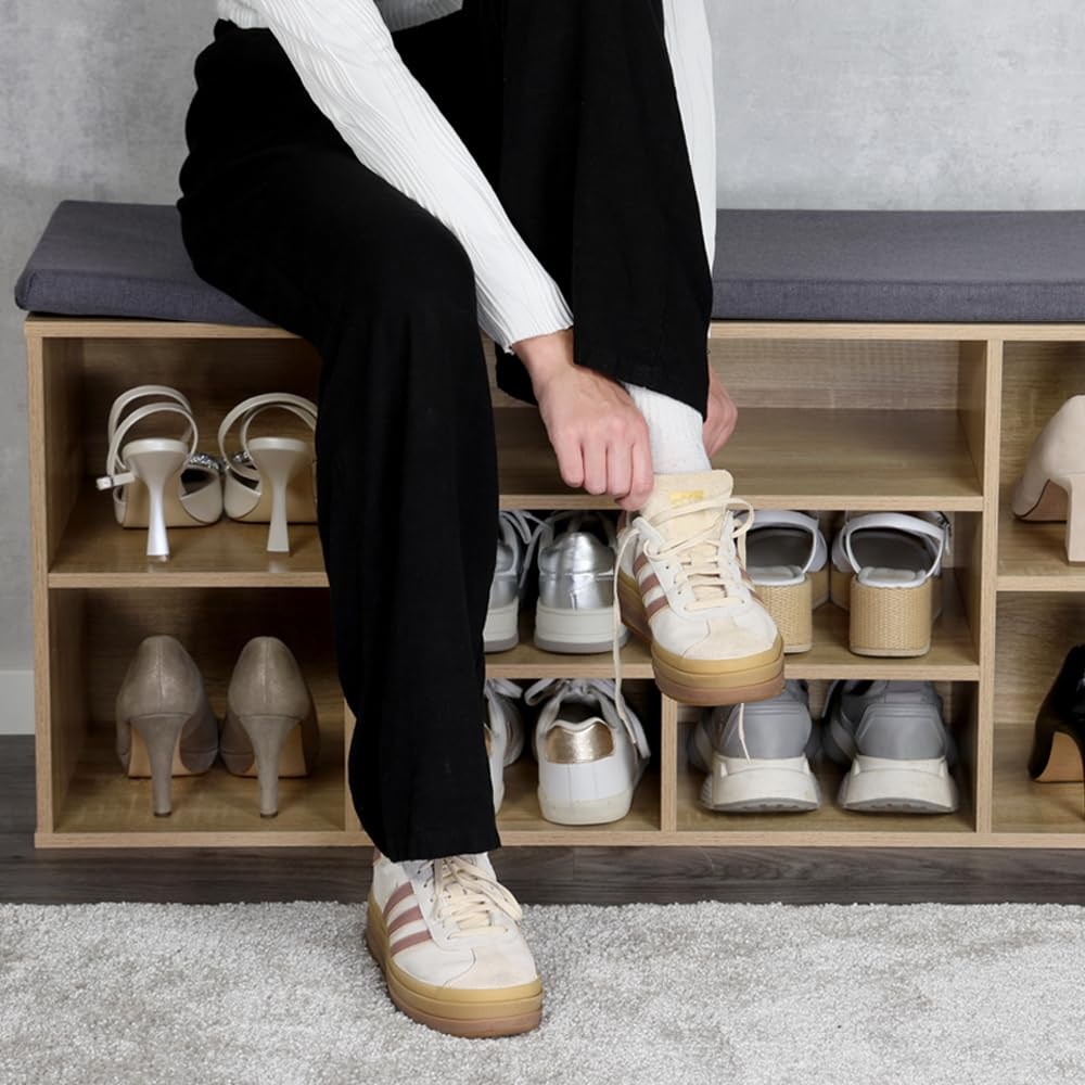 Eine Person sitzt auf einer Holzschuhbank und zieht beige-weiße Turnschuhe an.