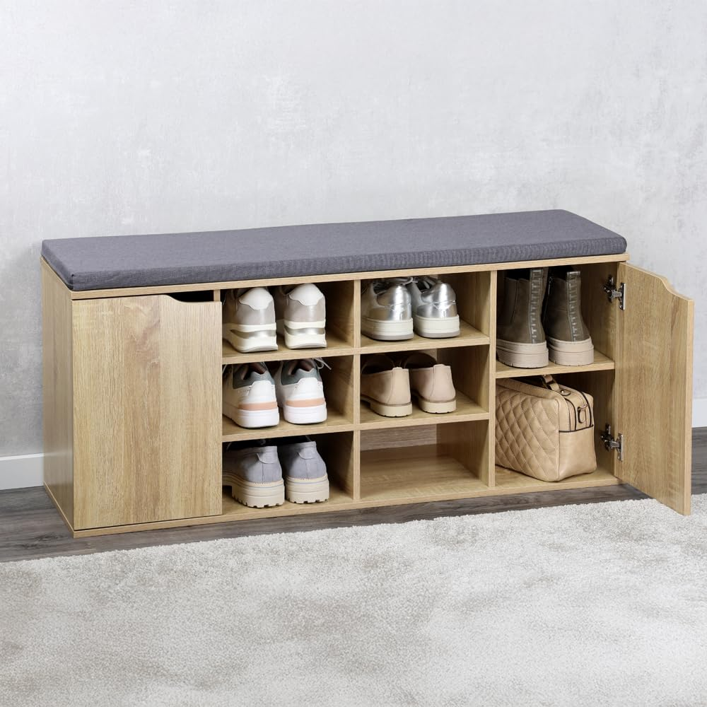Holzfarbene Schuhbank mit grauem Kissen, offenen Fächern voller Schuhe, geschlossener Tür und Tasche.