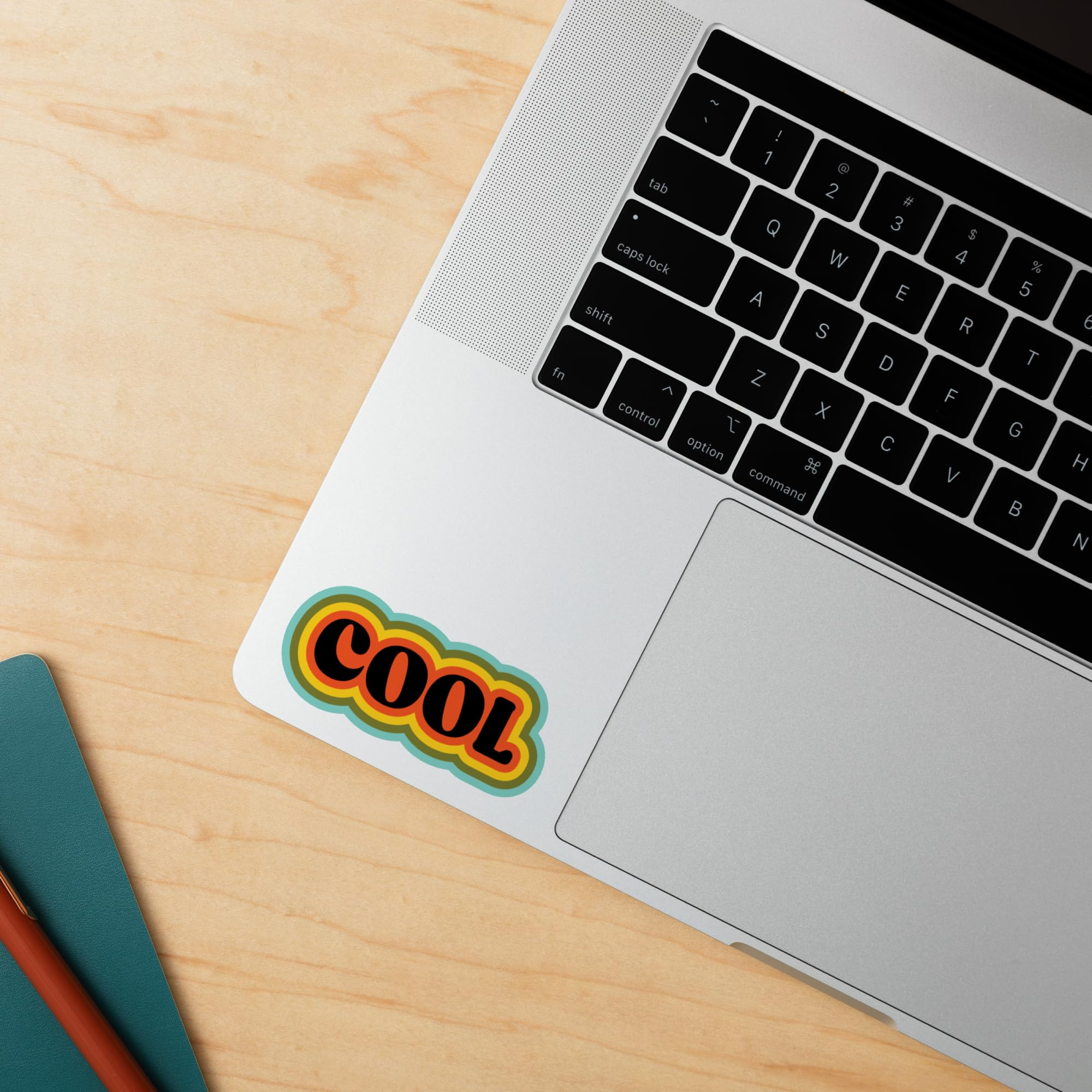 Autocollant COOL sur le repose-poignet d'un ordinateur portable argenté sur un bureau en bois.