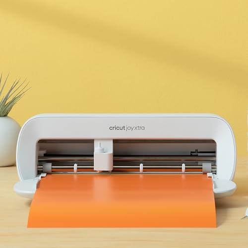 Une machine de découpe Cricut Joy Xtra blanche sur un bureau devant un fond jaune, avec un tapis orange.