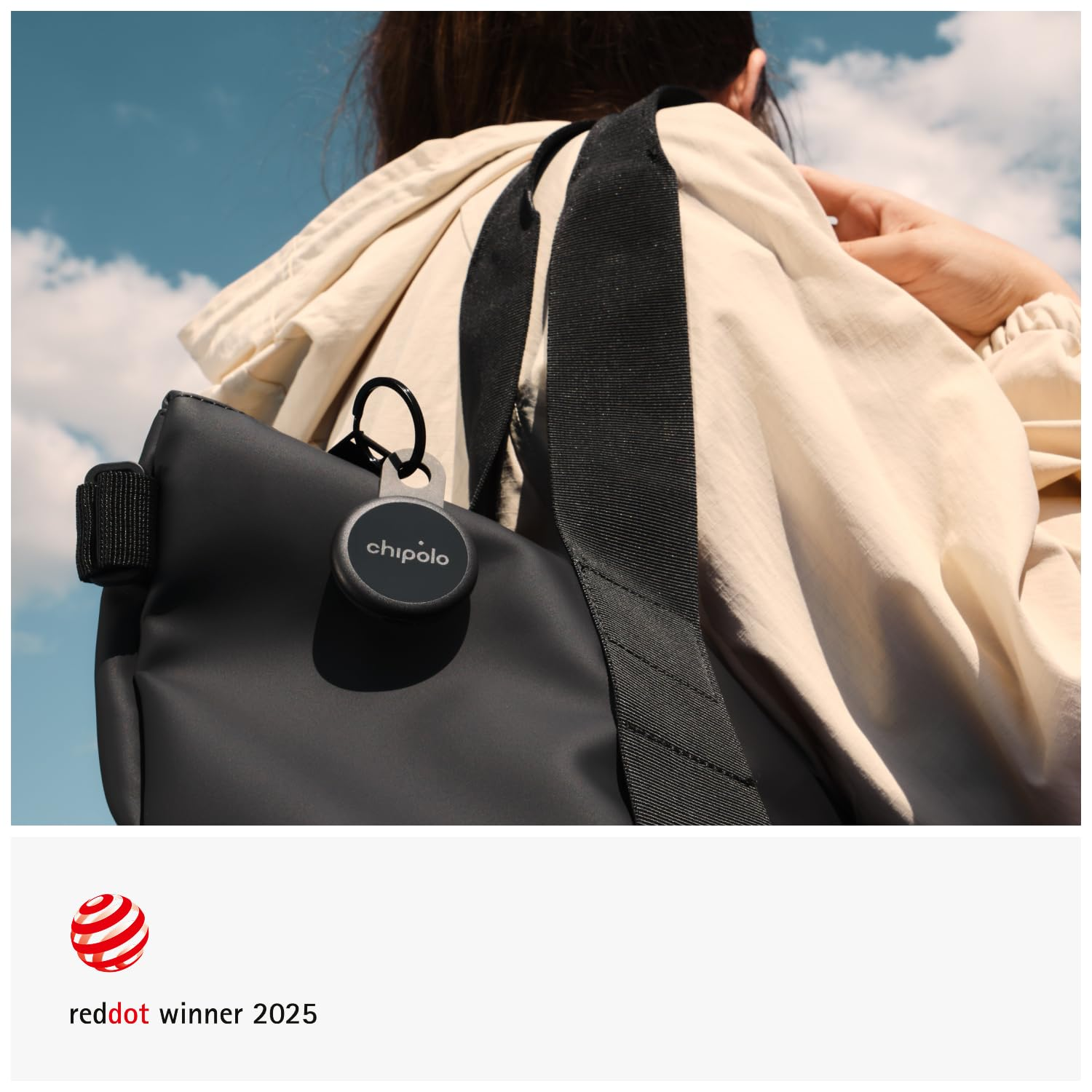 Eine Person mit Beiger Jacke trägt eine schwarze Tasche mit Chipolo-Tracker unter blauem Himmel mit Wolken.