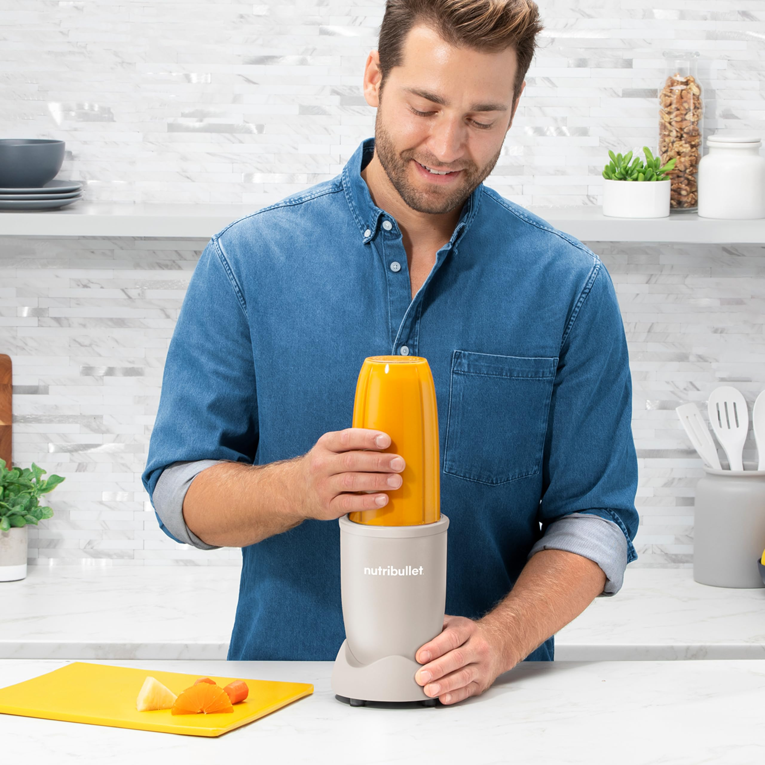 Ein Mann in einem blauen Hemd setzt den Becher auf eine NutriBullet-Küchenmaschine in einer Küche.