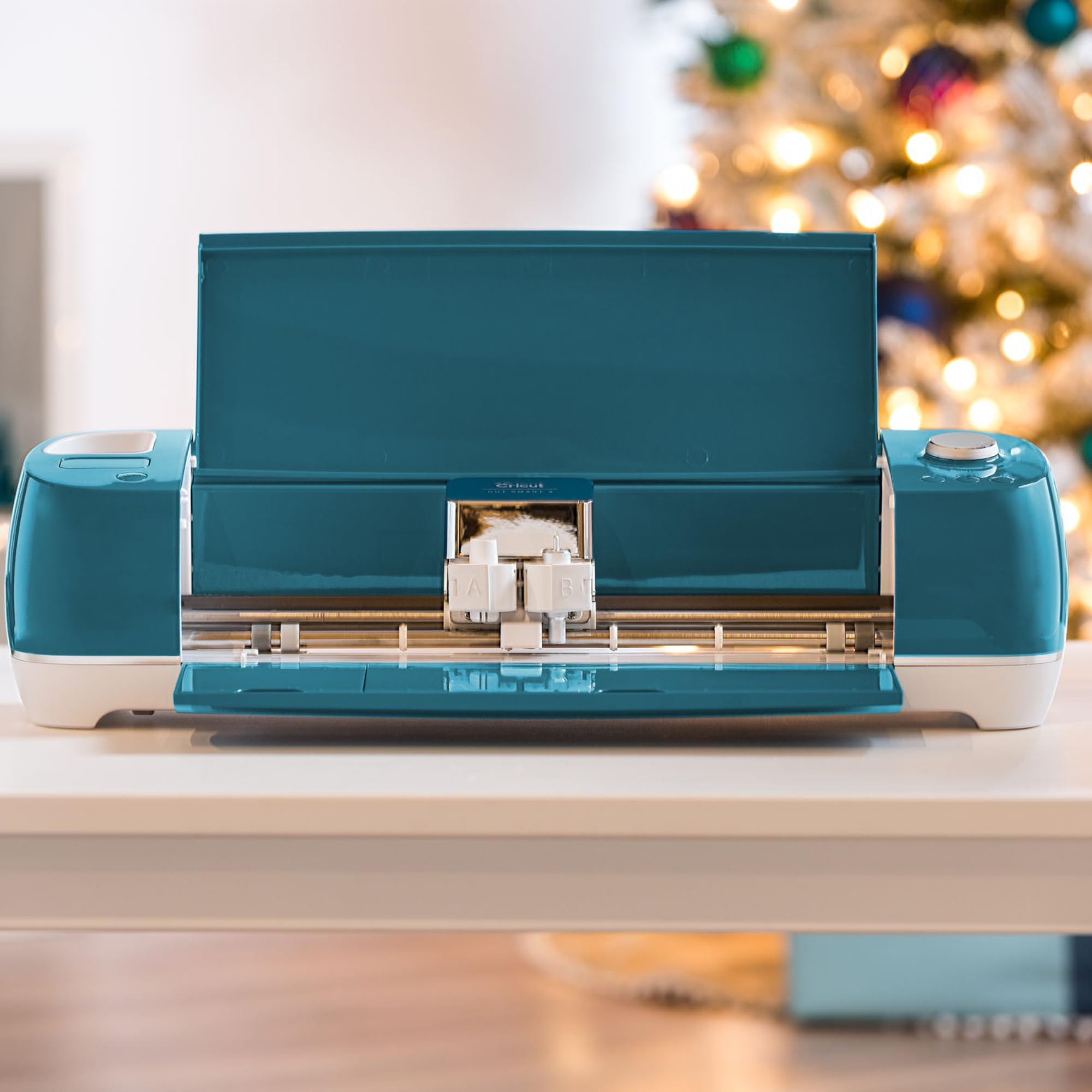 Machine de découpe sarcelle sur table blanche avec sapin de Noël illuminé.