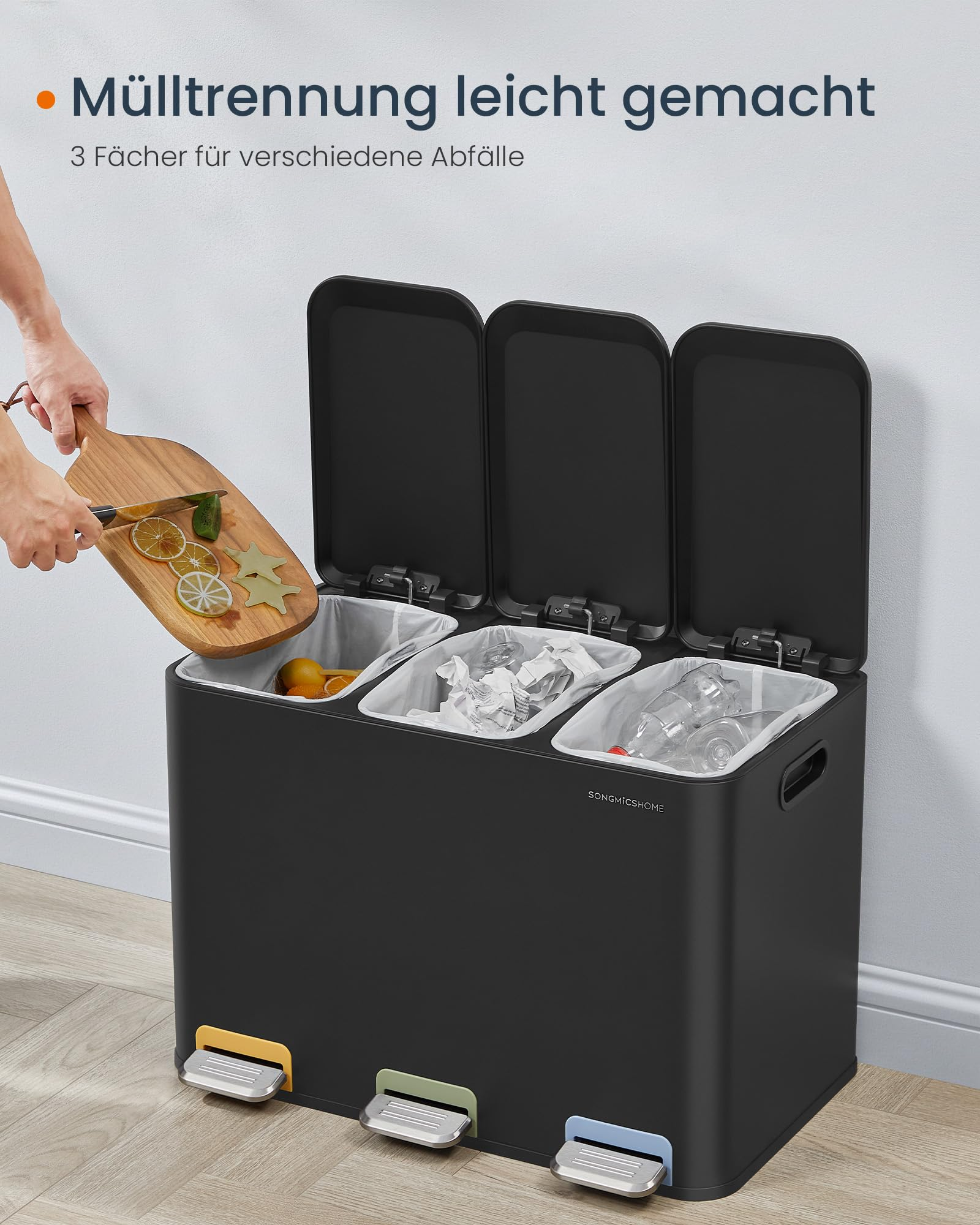 Ein schwarzer Mülleimer mit drei Fächern, geöffneten Deckeln und drei farbigen Fußpedalen für die Mülltrennung.