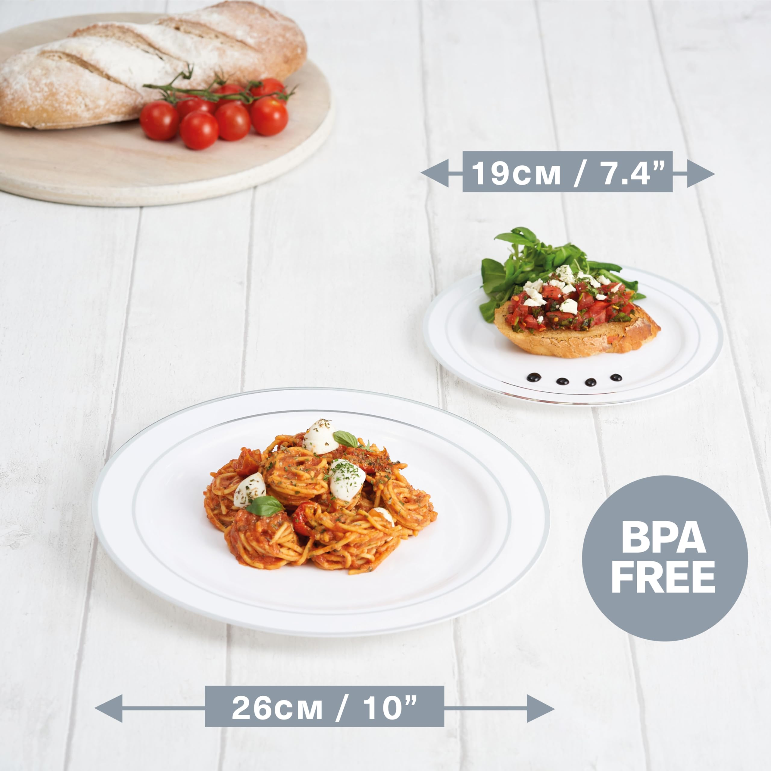 Due piatti bianchi con pasta e bruschetta su un tavolo di legno, accompagnati da pane e pomodori.