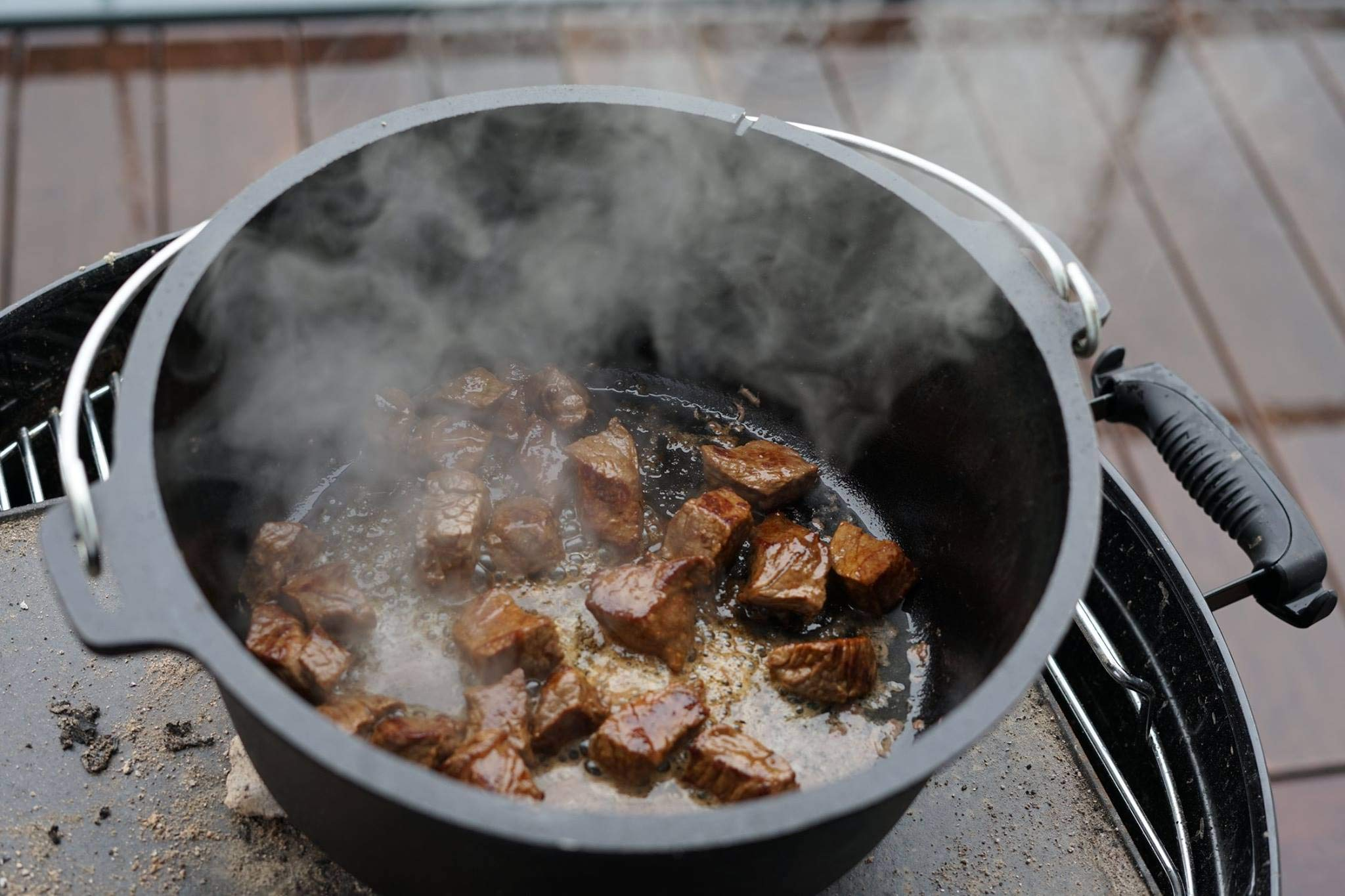 De la viande fumante cuit dans une poêle en fonte noire sur un gril.