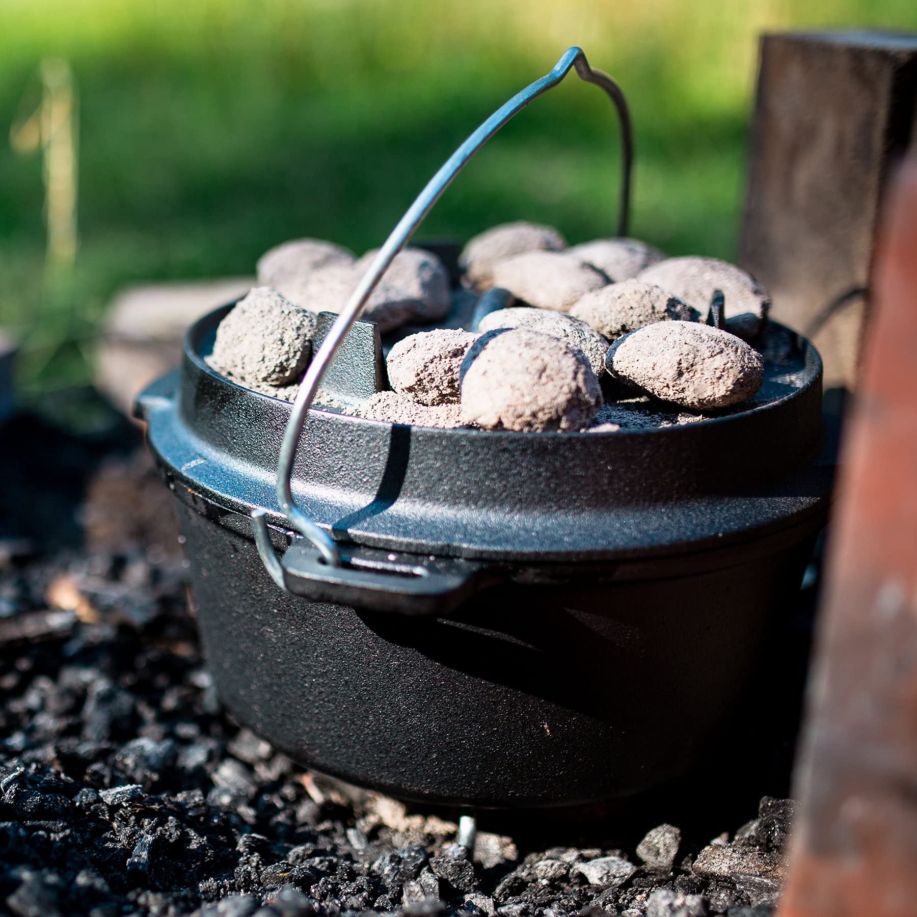Une cocotte en fonte noire avec des briquettes de charbon gris sur le couvercle se trouve à l'extérieur.
