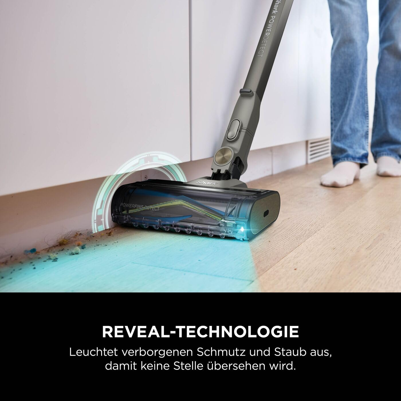 Ein grauer Staubsauger leuchtet mit blauem Licht auf Holzfußboden unter weißen Küchenmöbeln, um Schmutz zu zeigen.