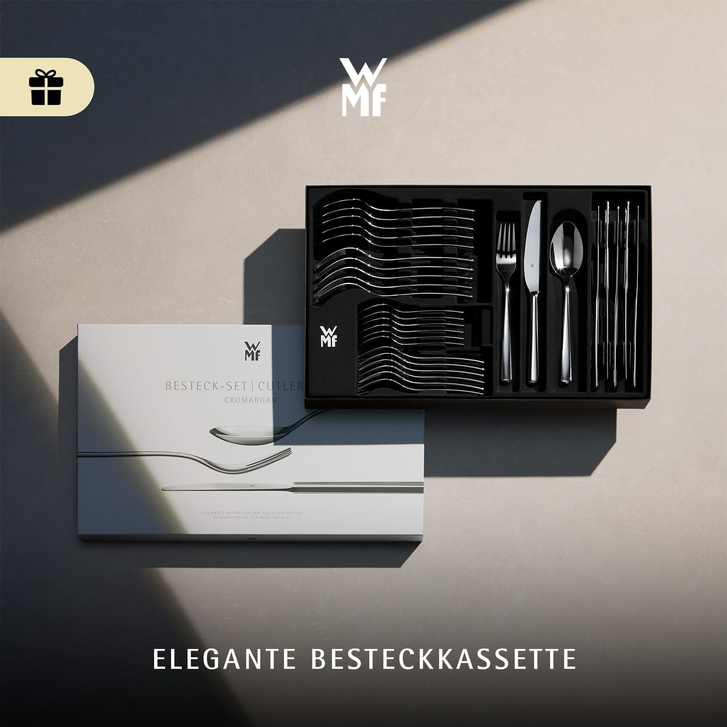 Un set de couverts WMF ouvert et son emballage blanc assorti sur une surface beige.