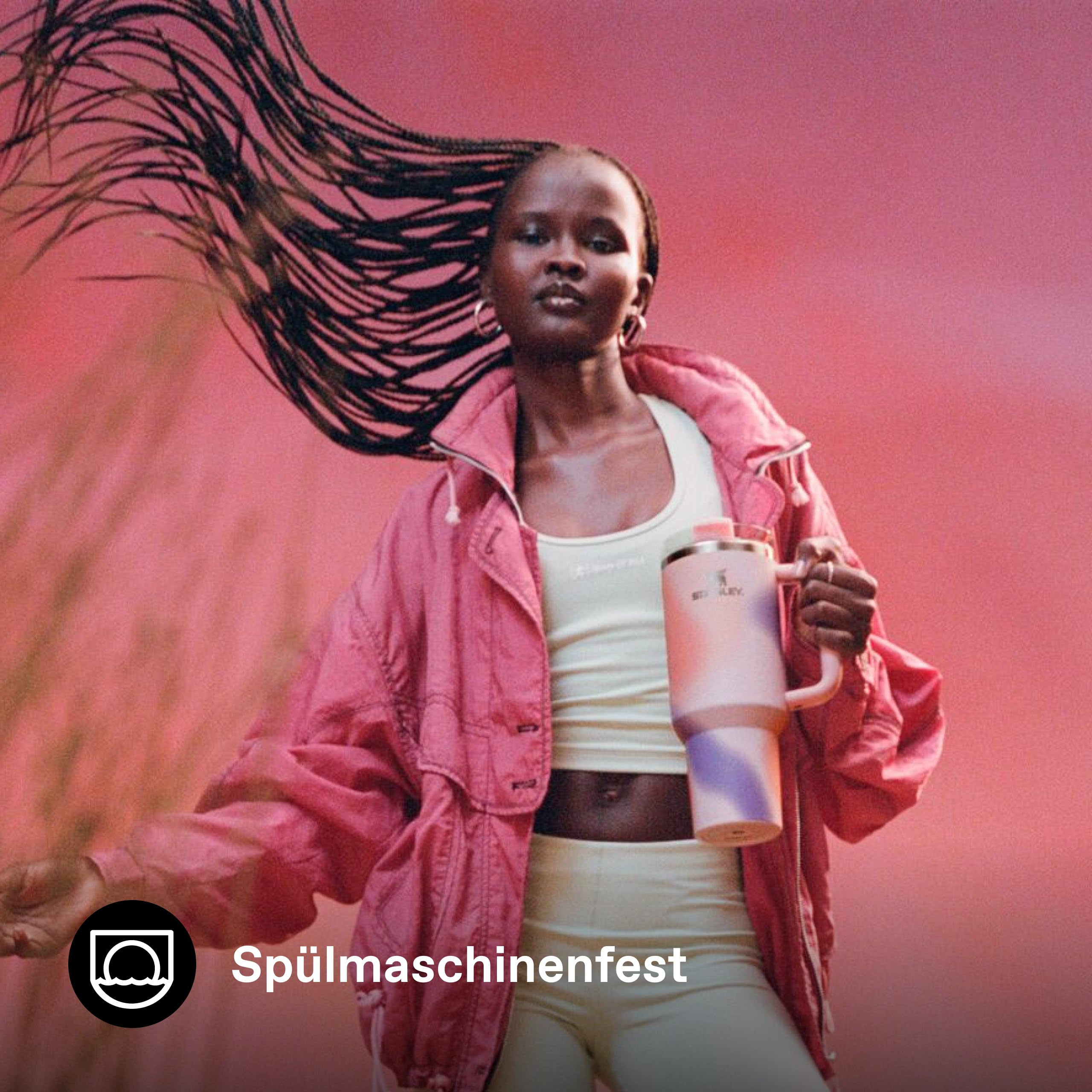 Eine Frau mit geflochtenen Haaren hält einen rosa-lila Becher vor rotem Hintergrund.