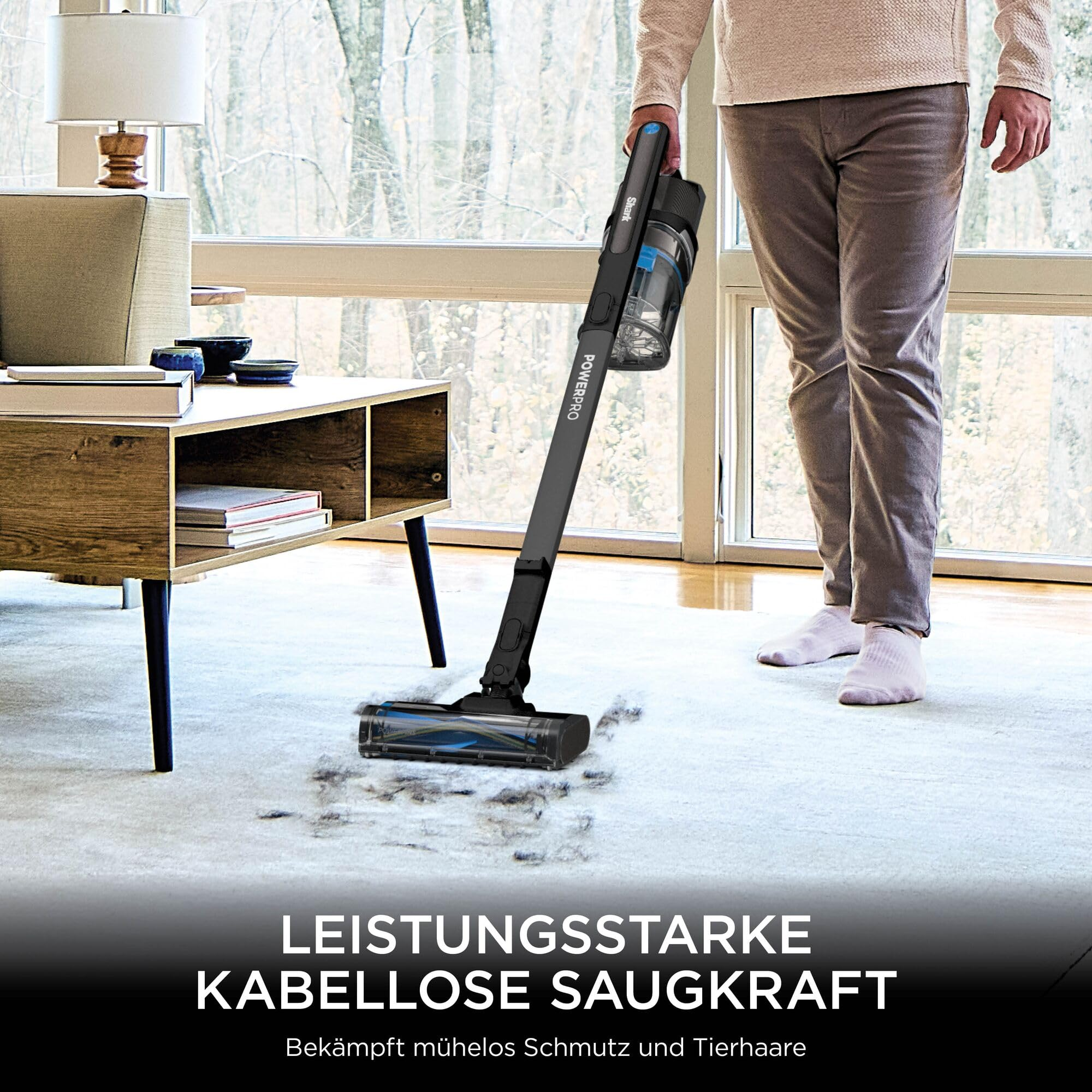 Eine Person benutzt einen schwarzen kabellosen Staubsauger auf einem Teppich.