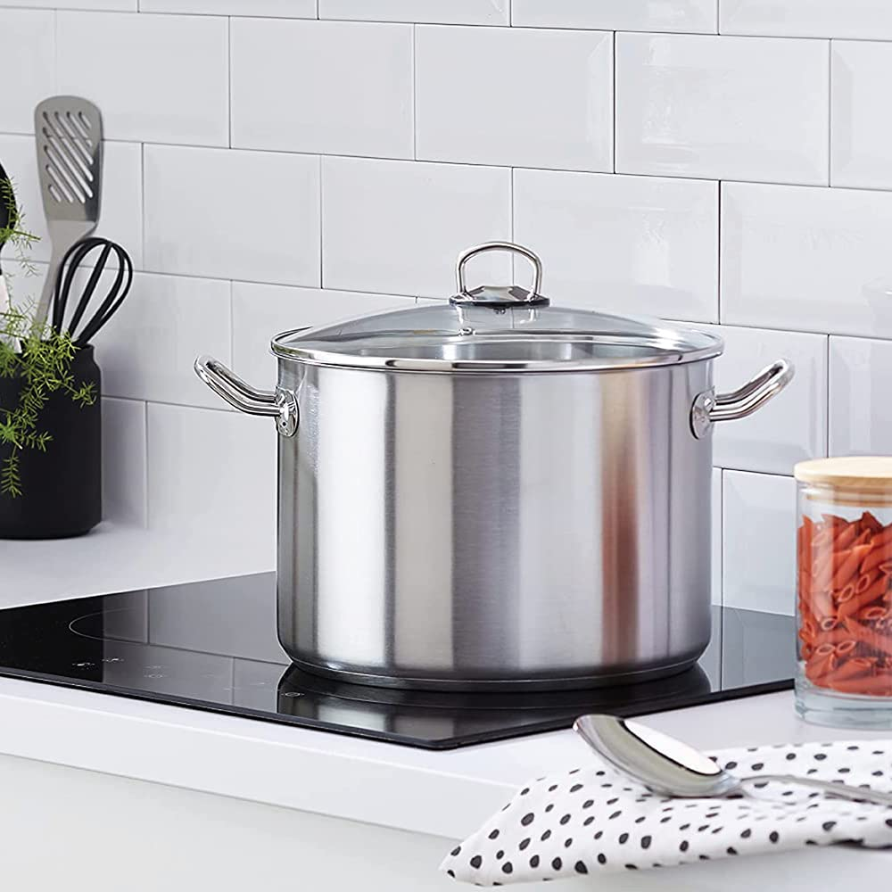 Une grande casserole en acier inoxydable avec couvercle en verre repose sur une plaque de cuisson en céramique.