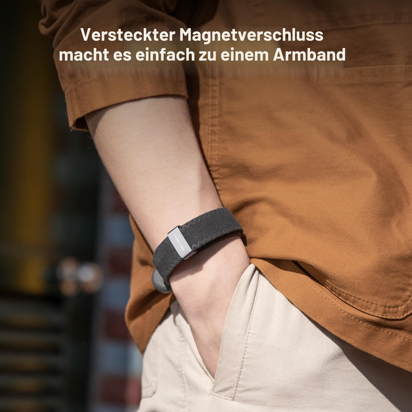 Person trägt ein dunkles Stoffarmband mit Magnetverschluss am Handgelenk, dazu braunes Hemd und helle Hose.