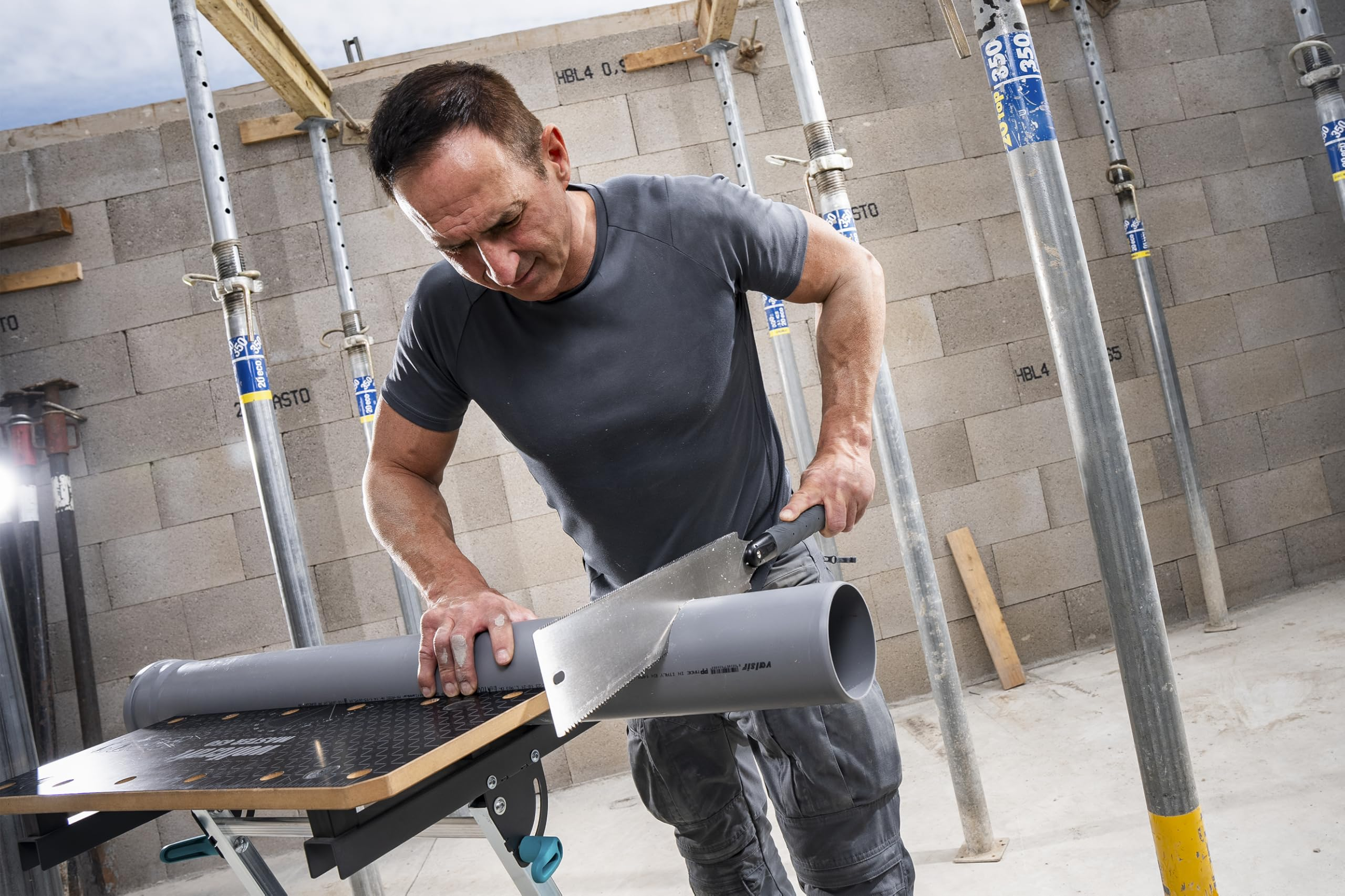 Ein Arbeiter sägt ein grau Rohrend auf einer Werkbank in einem Rohbau.