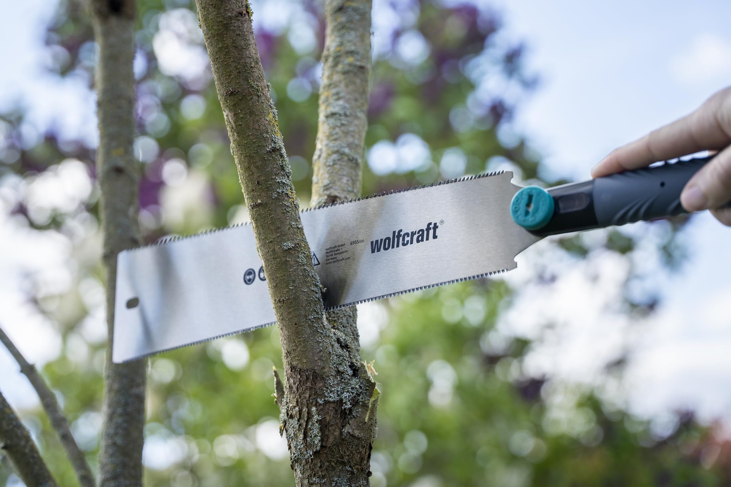 Eine Hand sägt mit einer Wolfcraft-Handsäge einen dünnen Ast im Garten ab.