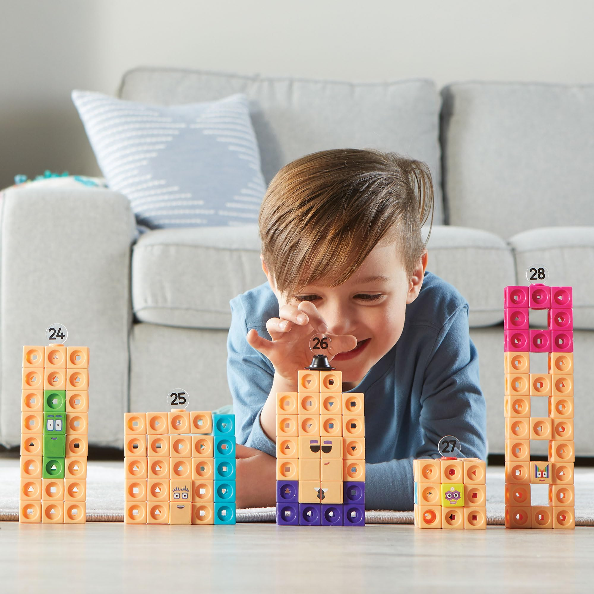 Un ragazzo si sdraia davanti a un divano, costruendo figure con blocchi colorati numerati.