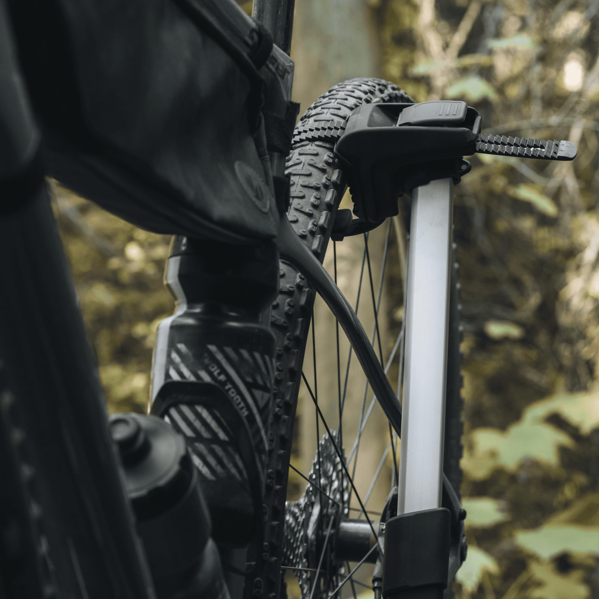 Primo piano di un telaio di bicicletta con borracce e borsa, montato su un portabici con sfondo boschivo.