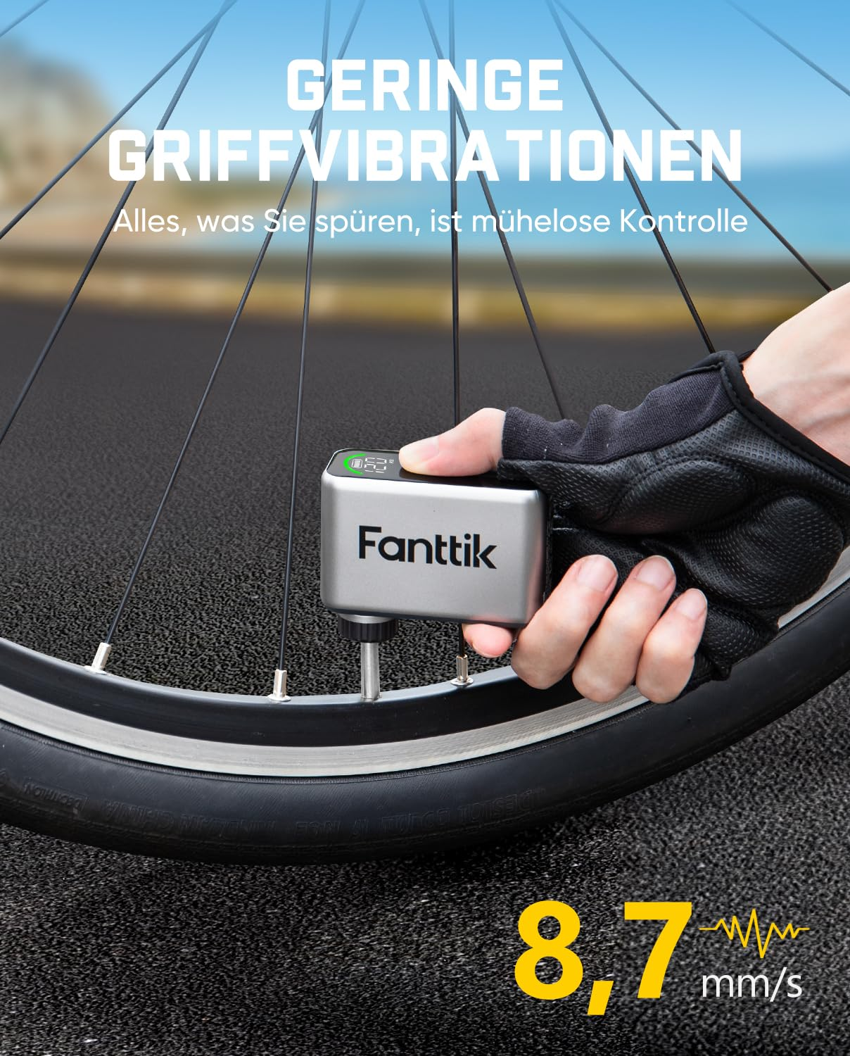 Main tenant une pompe à air Fanttik argentée sur un pneu de vélo, route en arrière-plan.