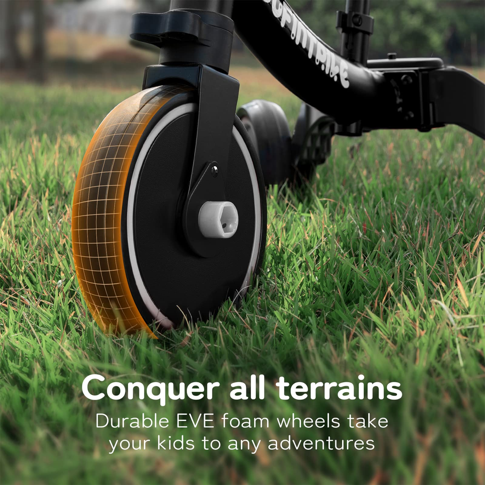 Gros plan sur une roue en mousse EVA noire et orange d'un tricycle pour enfants sur de l'herbe verte.