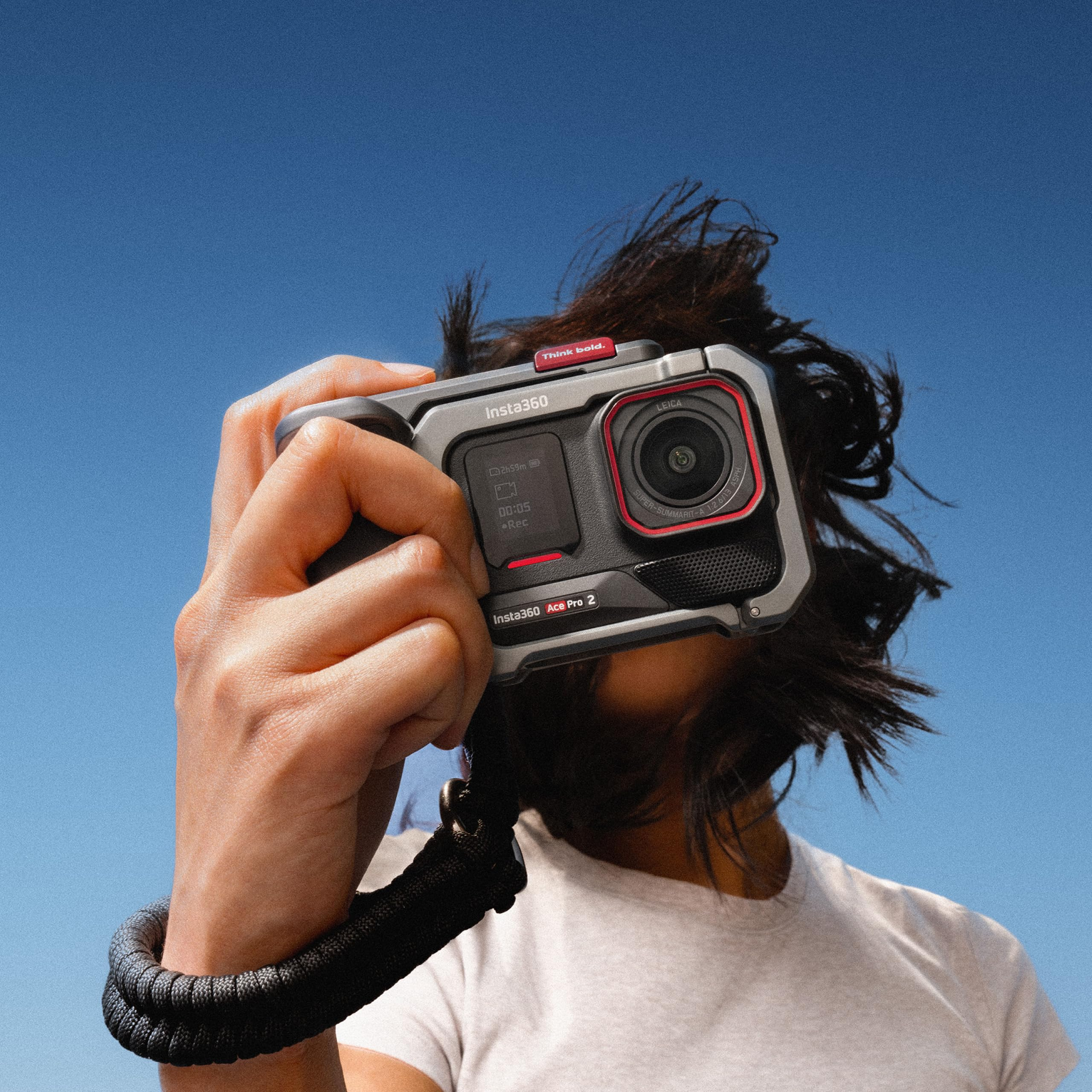 Eine Person im weißen T-Shirt hält eine Insta360 Ace Pro 2 Kamera vor das Gesicht vor blauem Himmel.