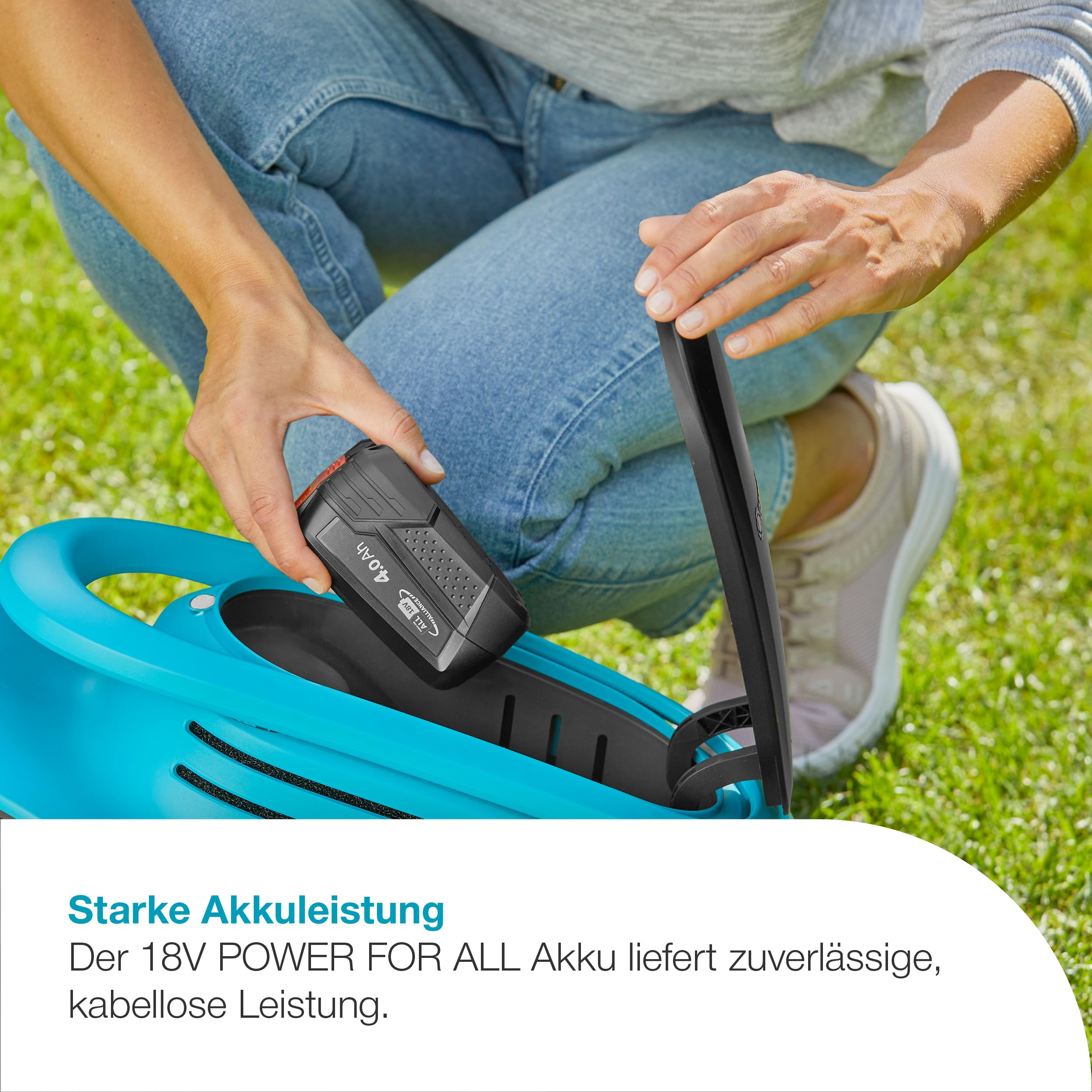 Une personne insère une batterie noire dans un outil de jardin bleu sur de l'herbe.