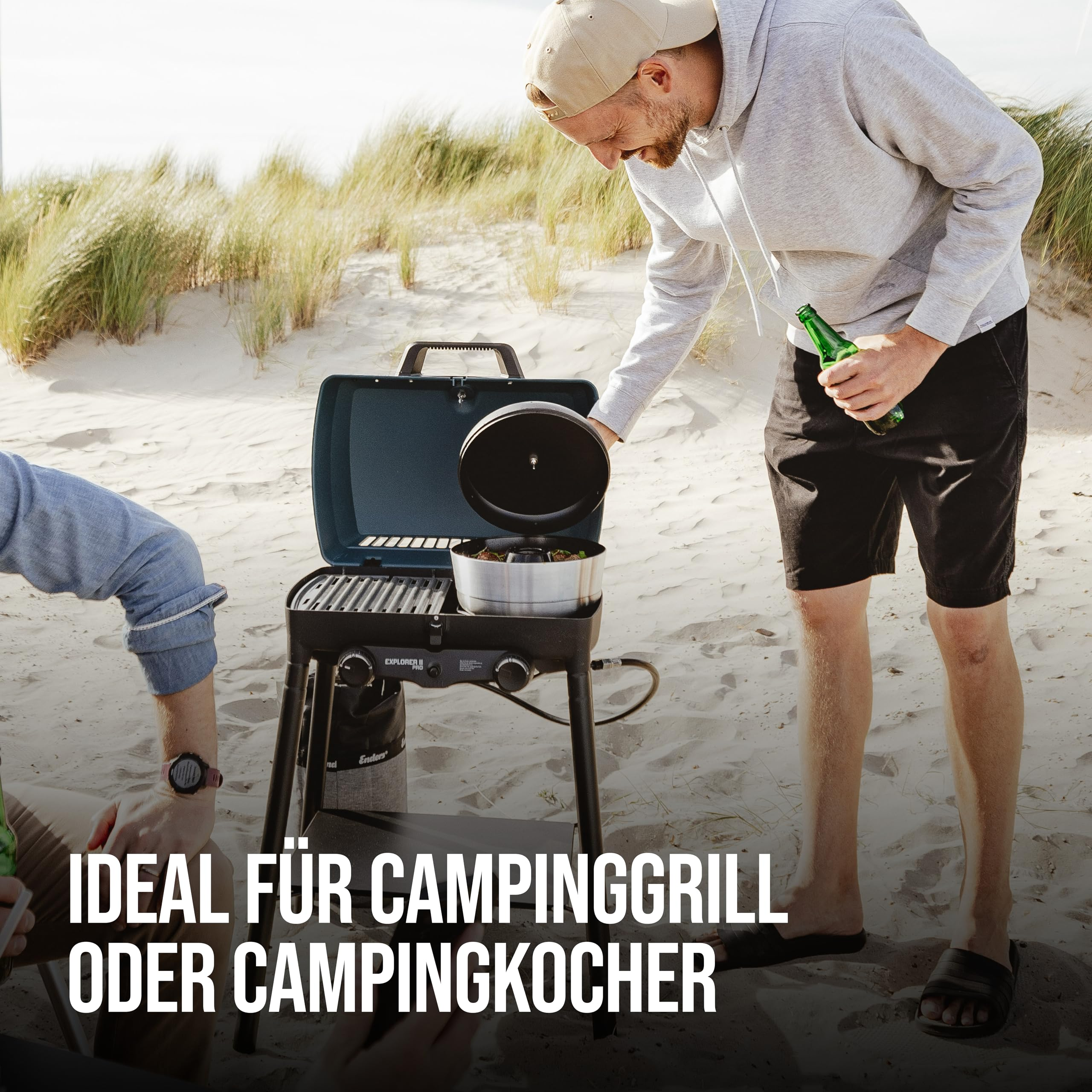 Un homme en sweat à capuche gris et casquette fait un barbecue sur une plage.