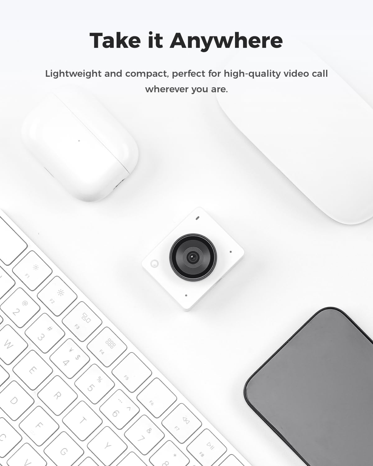 Una piccola telecamera bianca si trova su un tavolo bianco accanto a una tastiera e gadget.
