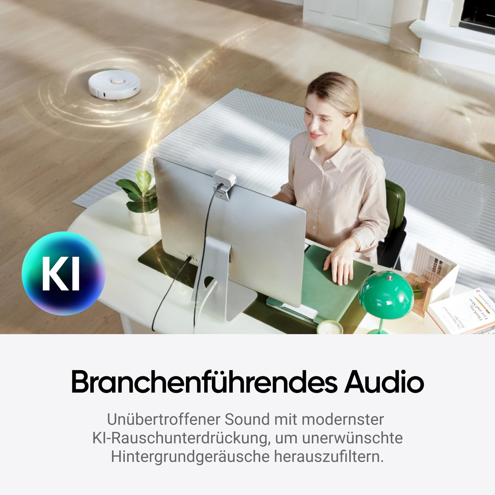 Eine Frau arbeitet am Computer, während im Hintergrund ein Saugroboter saugt.