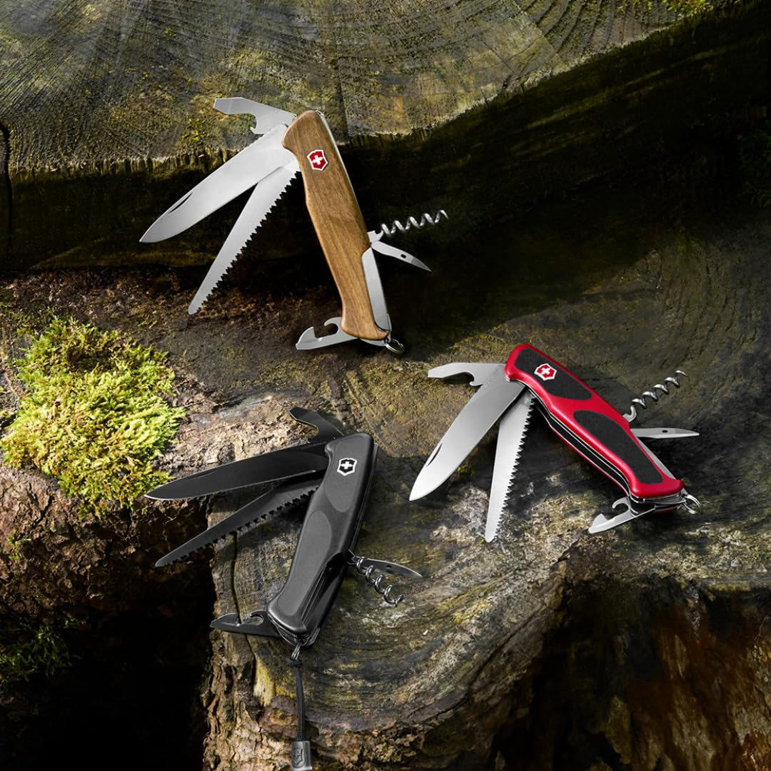 Drei Schweizer Taschenmesser mit Holzbeschalung, rotem sowie schwarzem Griff liegen auf einem moosigen Baumstumpf.