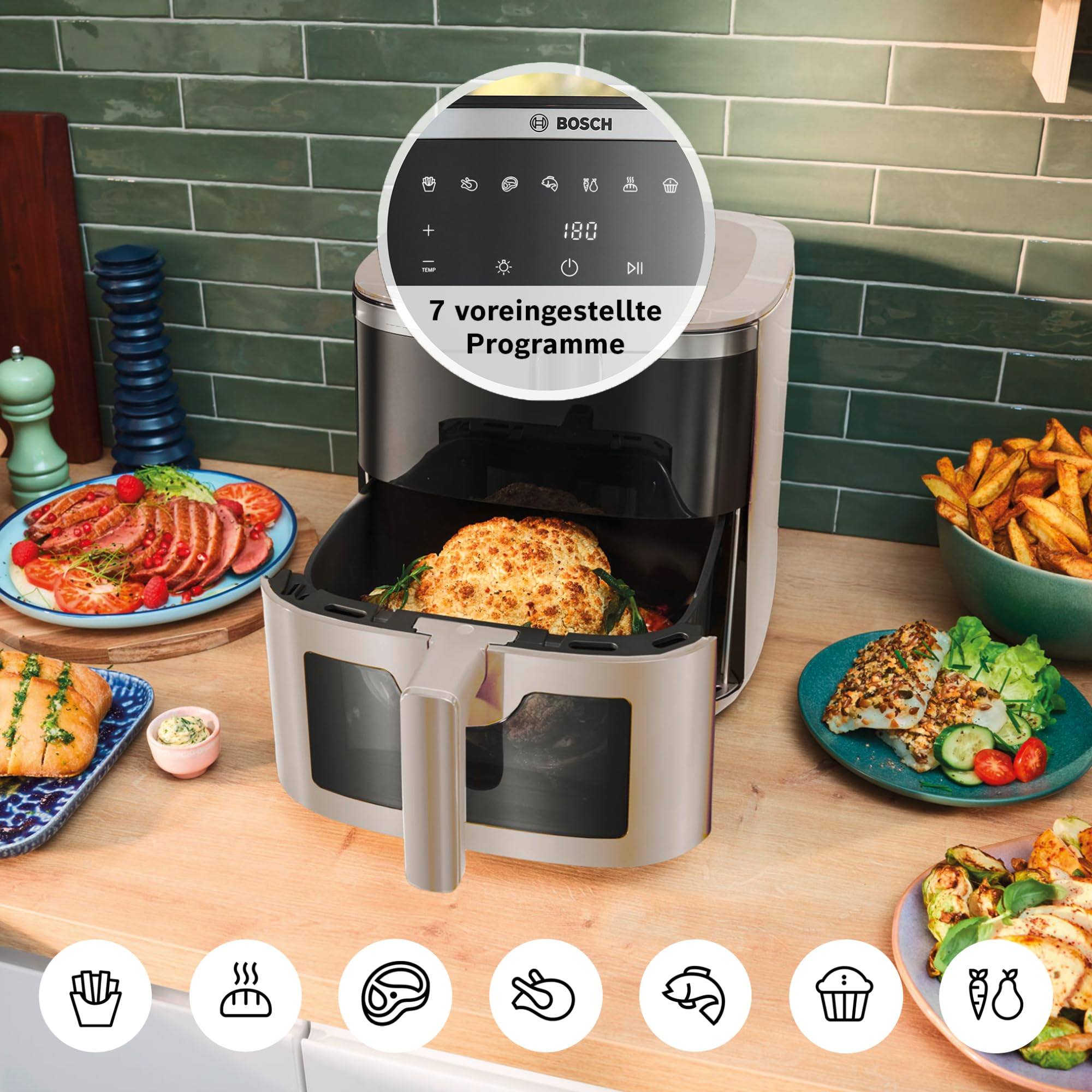 Una friggitrice ad aria Bosch su un piano cucina con cassetto aperto contenente cibo, circondata da vari piatti.