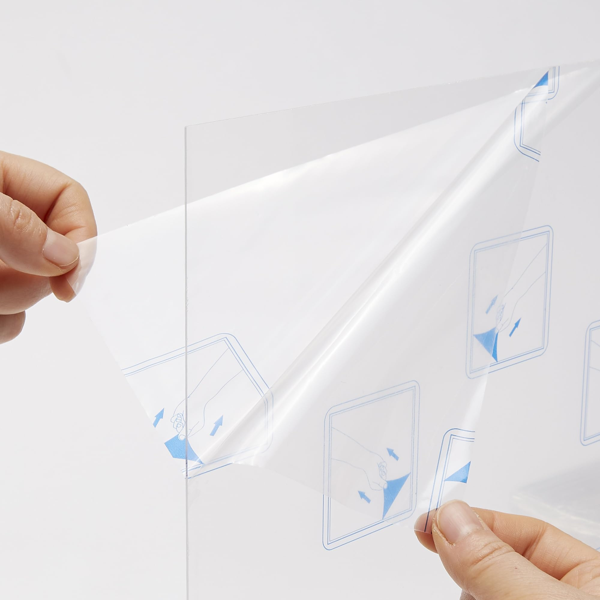 Hände ziehen eine transparente Schutzfolie von einer klaren Platte ab, die mit blauen Symbolen bedruckt ist.